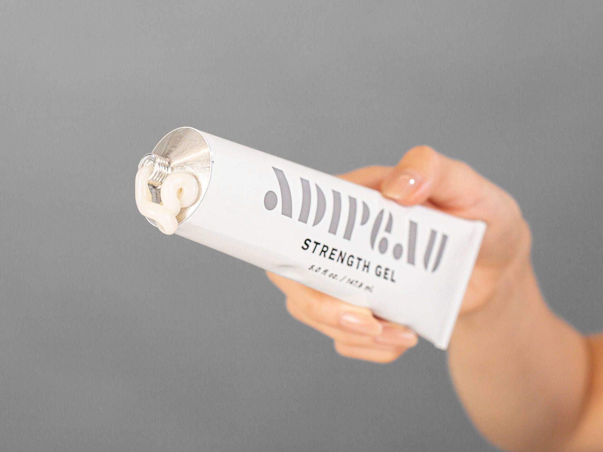 Laziza from LAZ Skincare's hand holding a tube of Adipeau Strength Gel on a neutral background