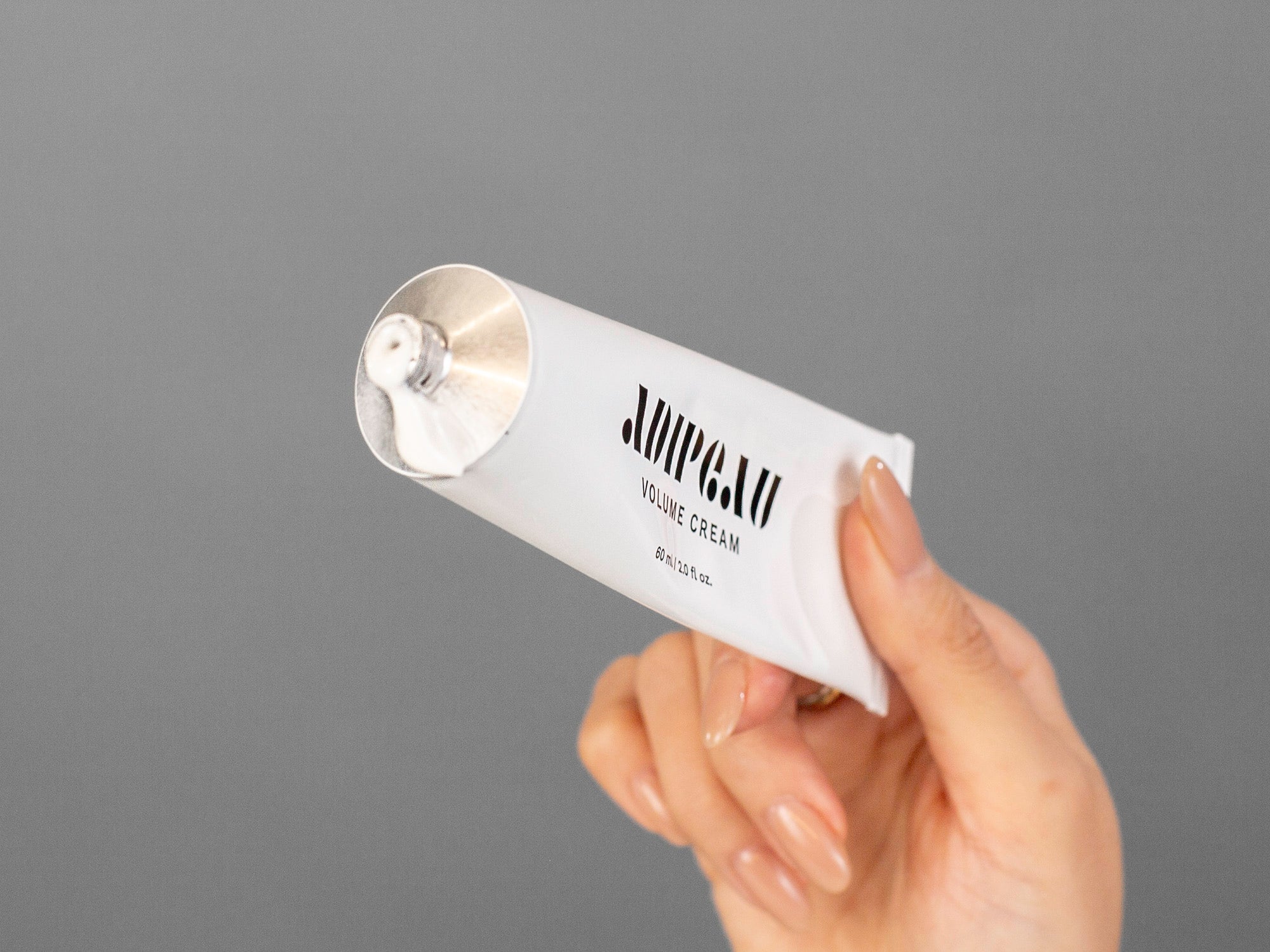 Laziza from LAZ Skincare's hand holding a tube of Adipeau Volume Cream on a neutral background