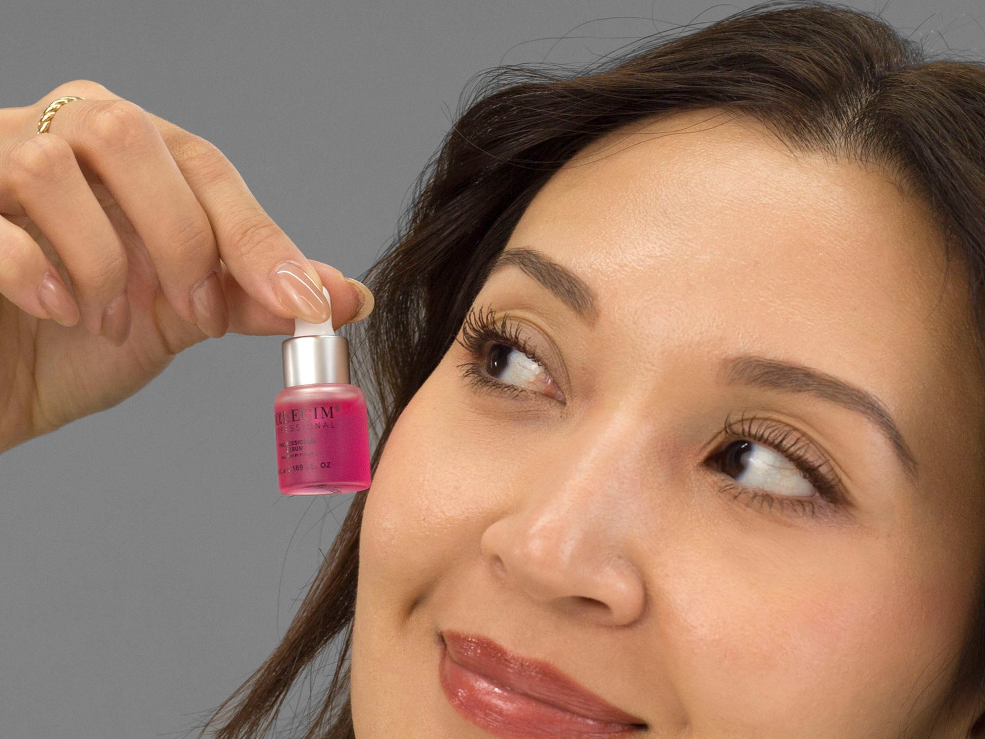 Laziza from LAZ Skincare holding a bottle from Calecim Professional Serum up to her face