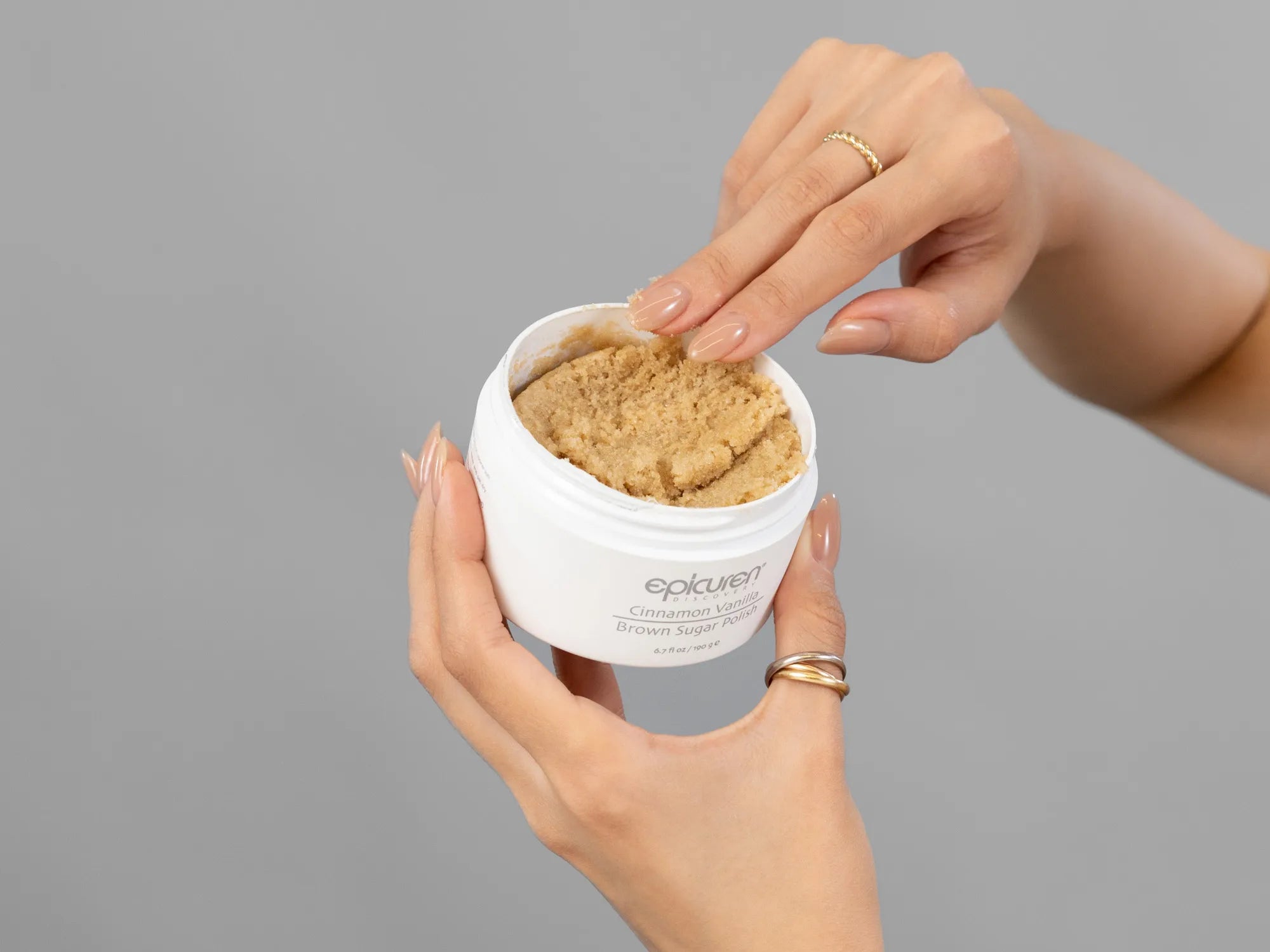 Closeup of Laziza from LAZ Skincare holding up a bottle of Epicuren Cinnamon Vanilla Brown Sugar Polish
