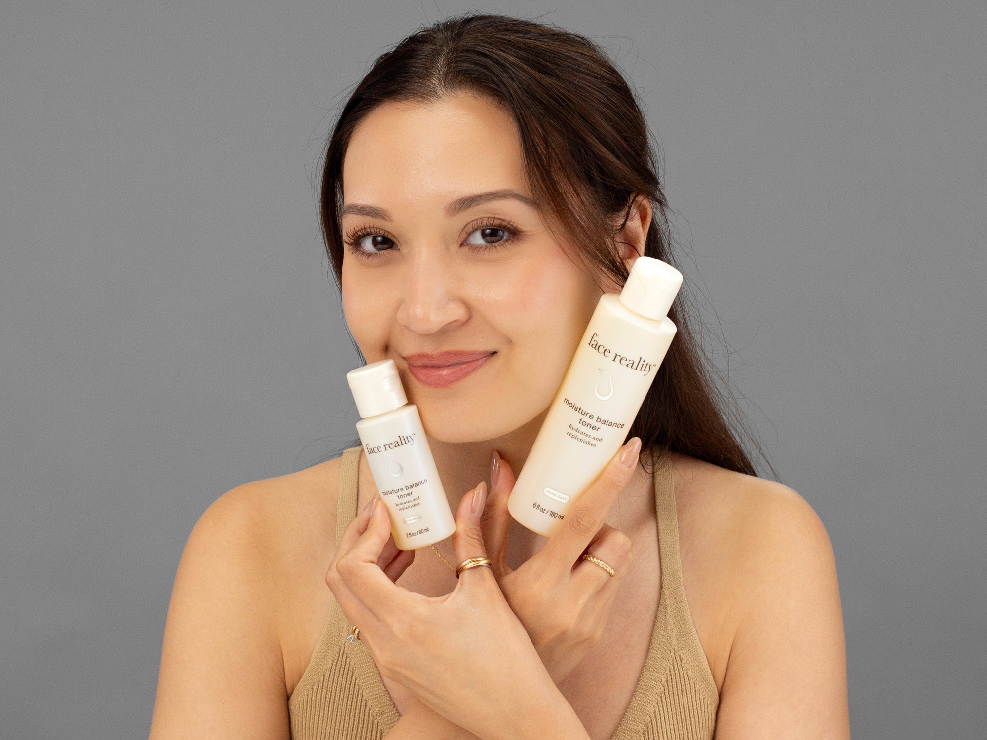 Laziza from LAZ Skincare holding both sizes of Face Reality Moisture Balance Toner bottles up to her face