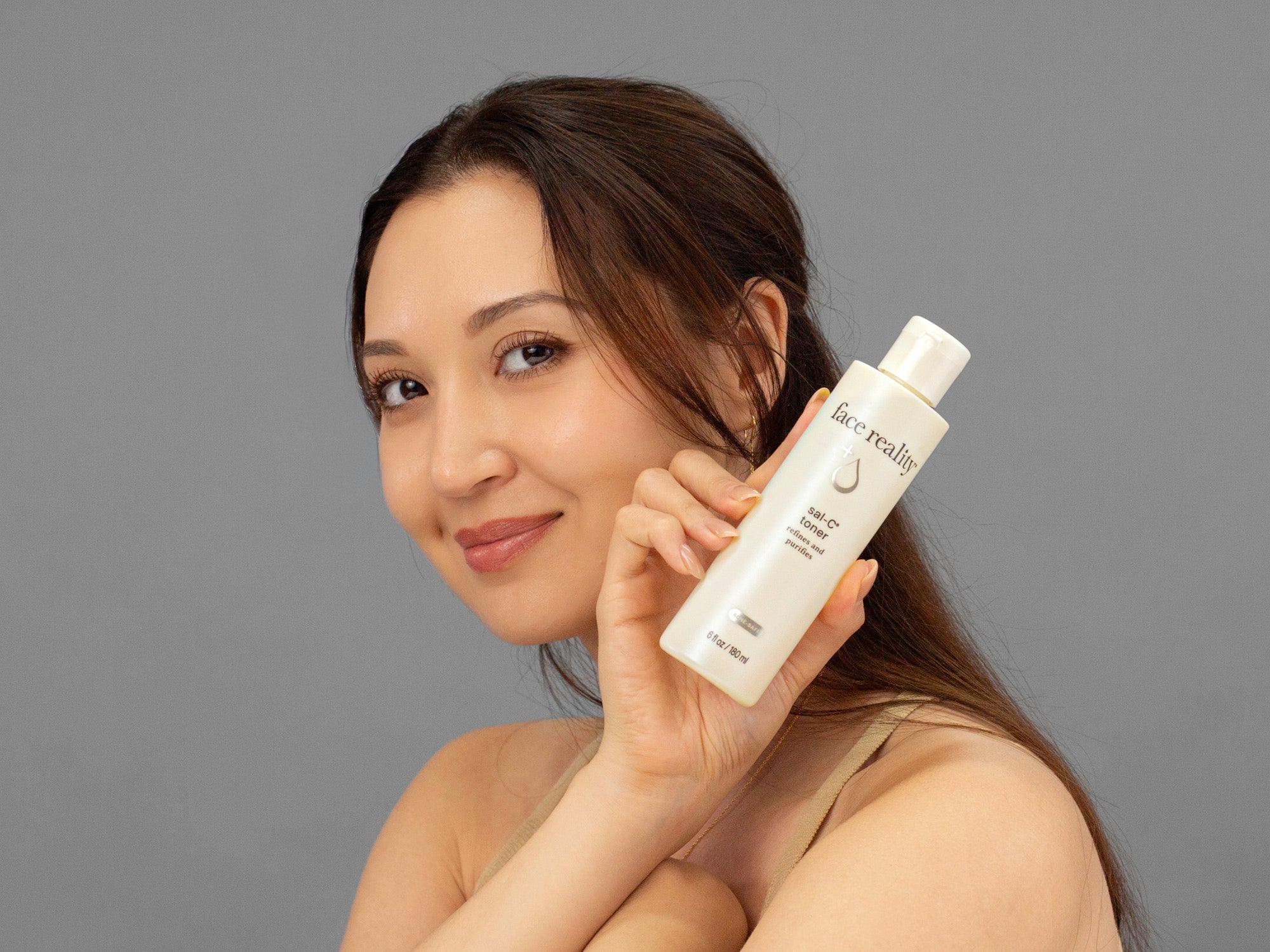 Laziza from LAZ Skincare holding a bottle of Face Reality Sal-C Toner up to her face