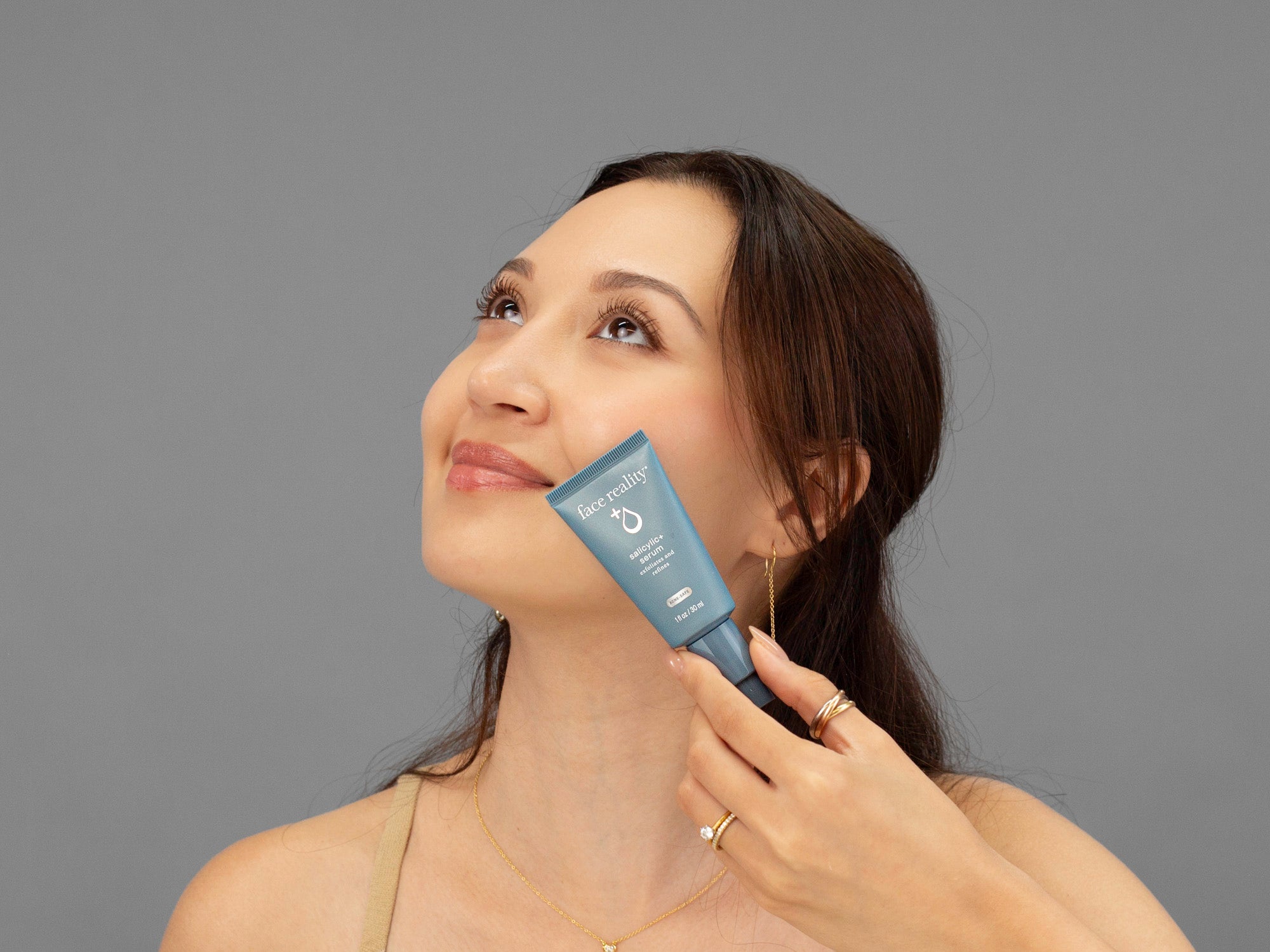 Laziza from LAZ Skincare holding a bottle of Face Reality Salicylic+ Serum up to her face