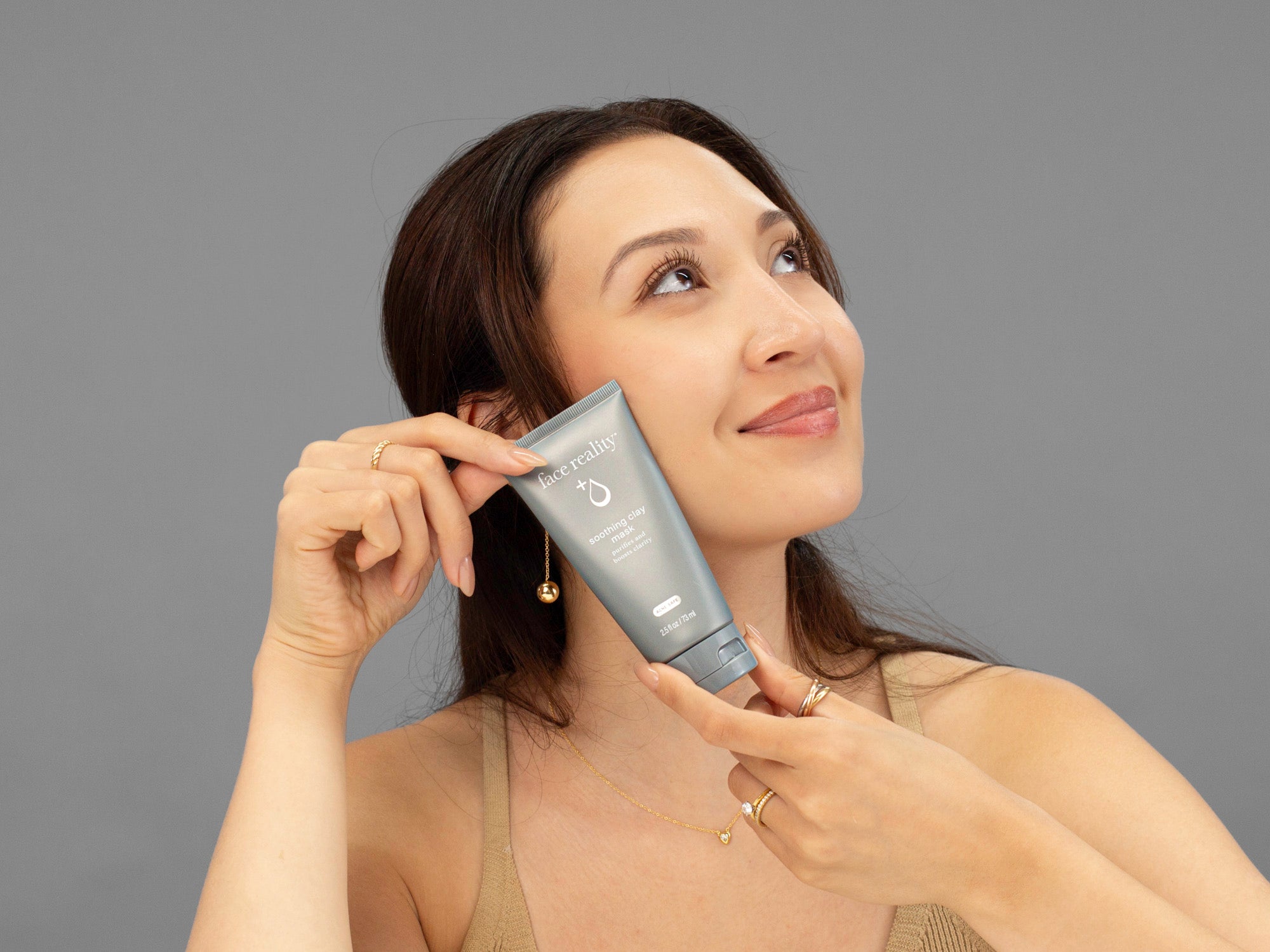 Laziza from LAZ Skincare holding a bottle of Face Reality Soothing Clay Mask up to her face
