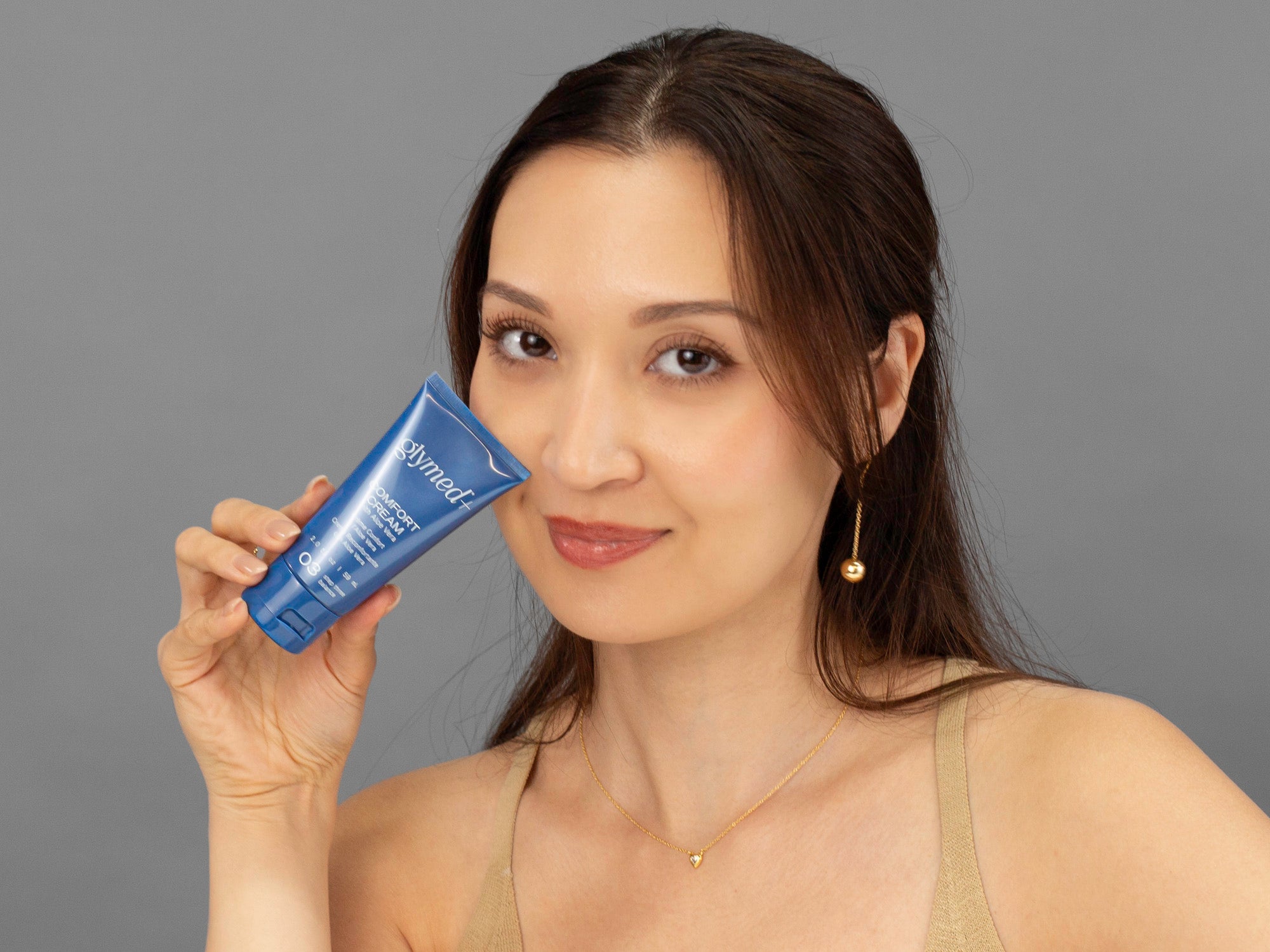 Laziza from LAZ Skincare holding a tube of GlyMed Comfort Cream up to her face