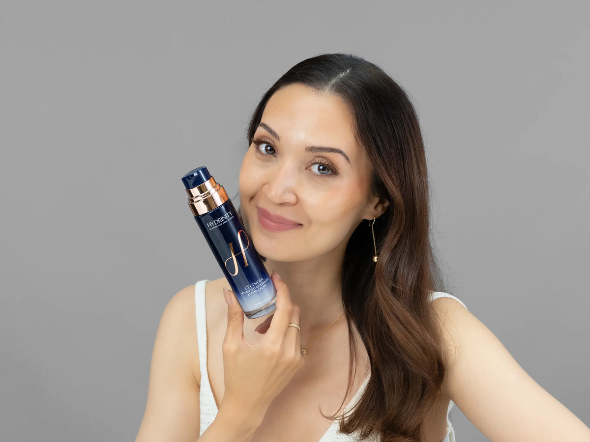 Laziza from LAZ Skincare holding a bottle of Hydrinity CELTHERA Advanced Overnight Repair Cream up to her face