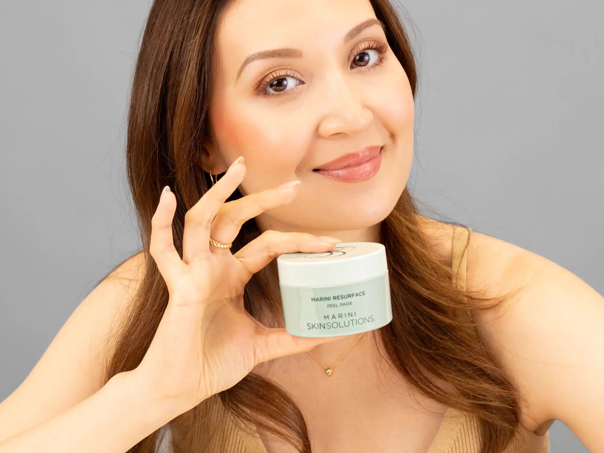 Laziza from LAZ Skincare holding a bottle of Marini SkinSolutions Marini Resurface Peel Pads up to her face