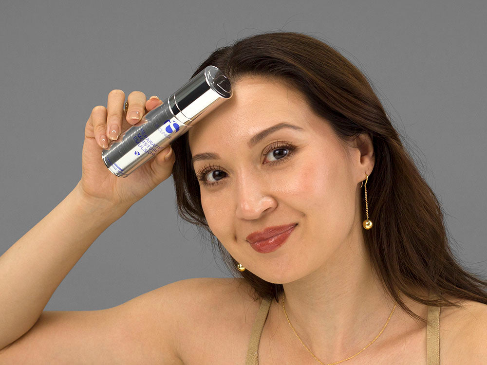 Laziza from LAZ Skincare holding a bottle of iS Clinical Reparative Moisture Emulsion up to her face