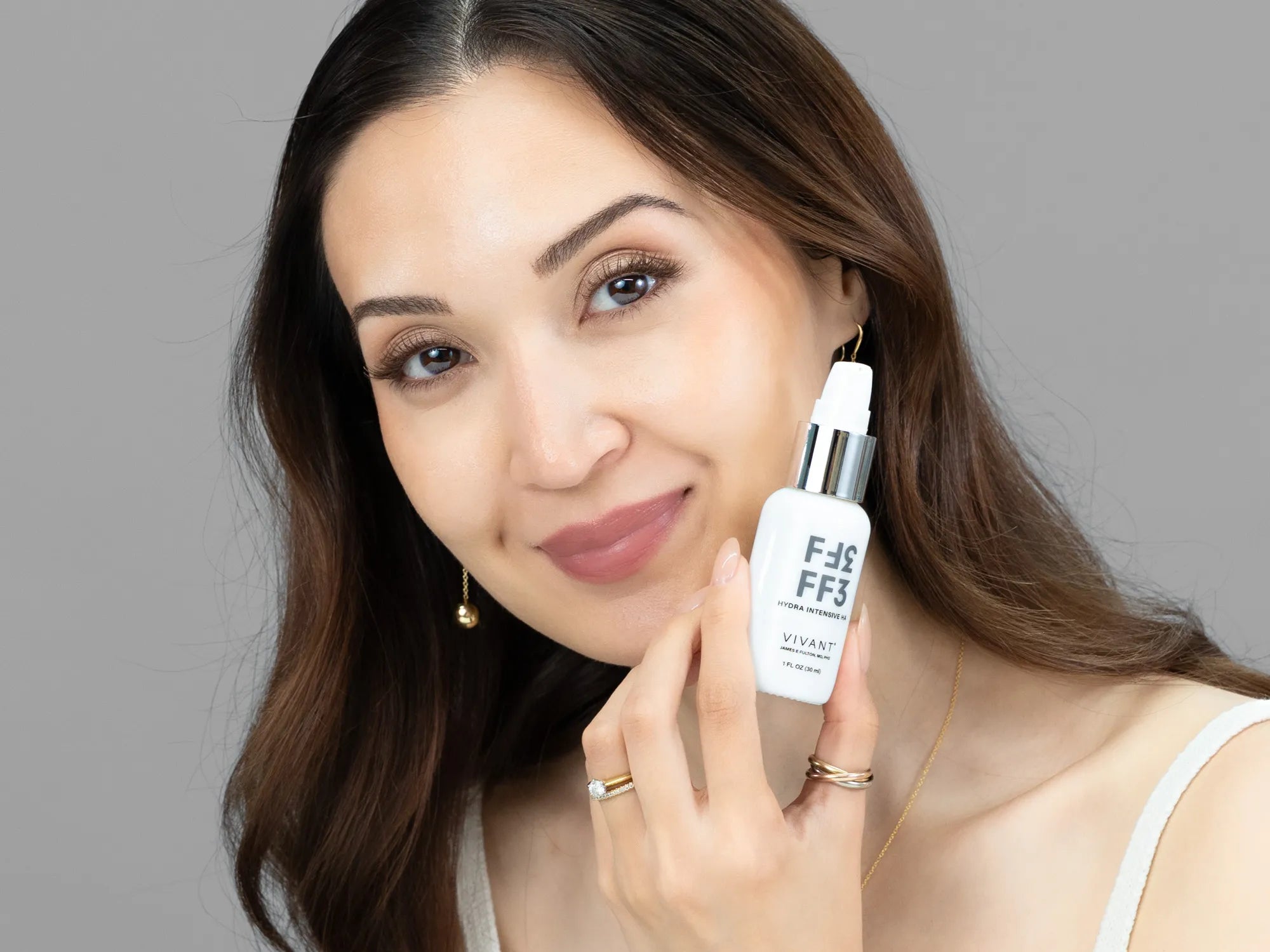 Laziza from LAZ Skincare holding a bottle of Vivant FF3 Hydra Intensive HA up to her face