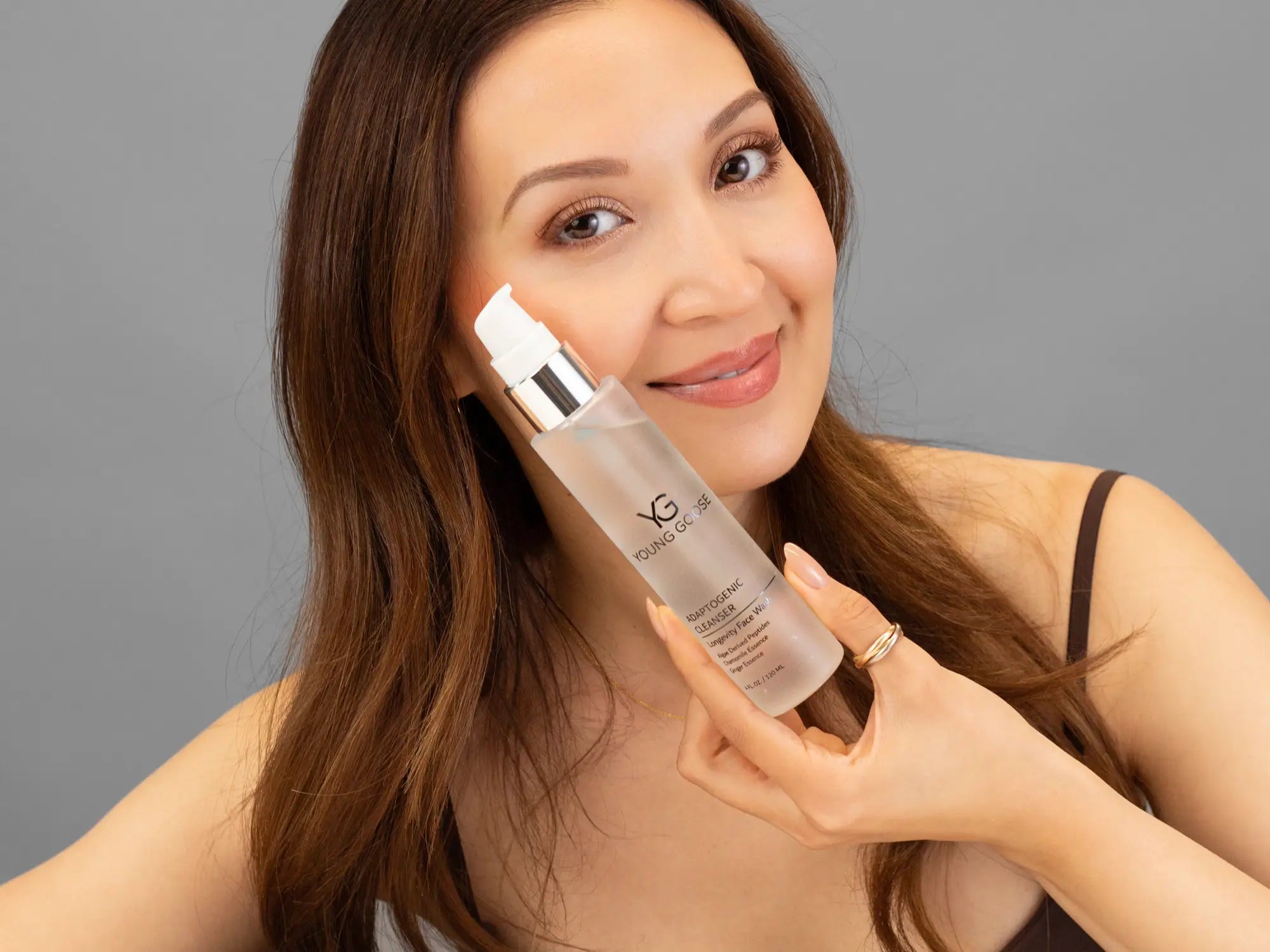 Laziza from LAZ Skincare holding a bottle of Young Goose Adaptogenic Cleanser up to her face