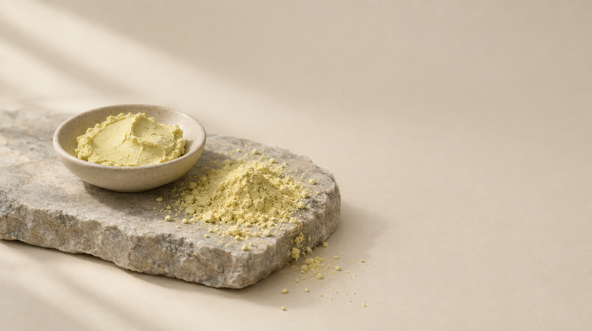 A shallow dish of pale yellow paste beside fine mineral powder on a stone slab.
