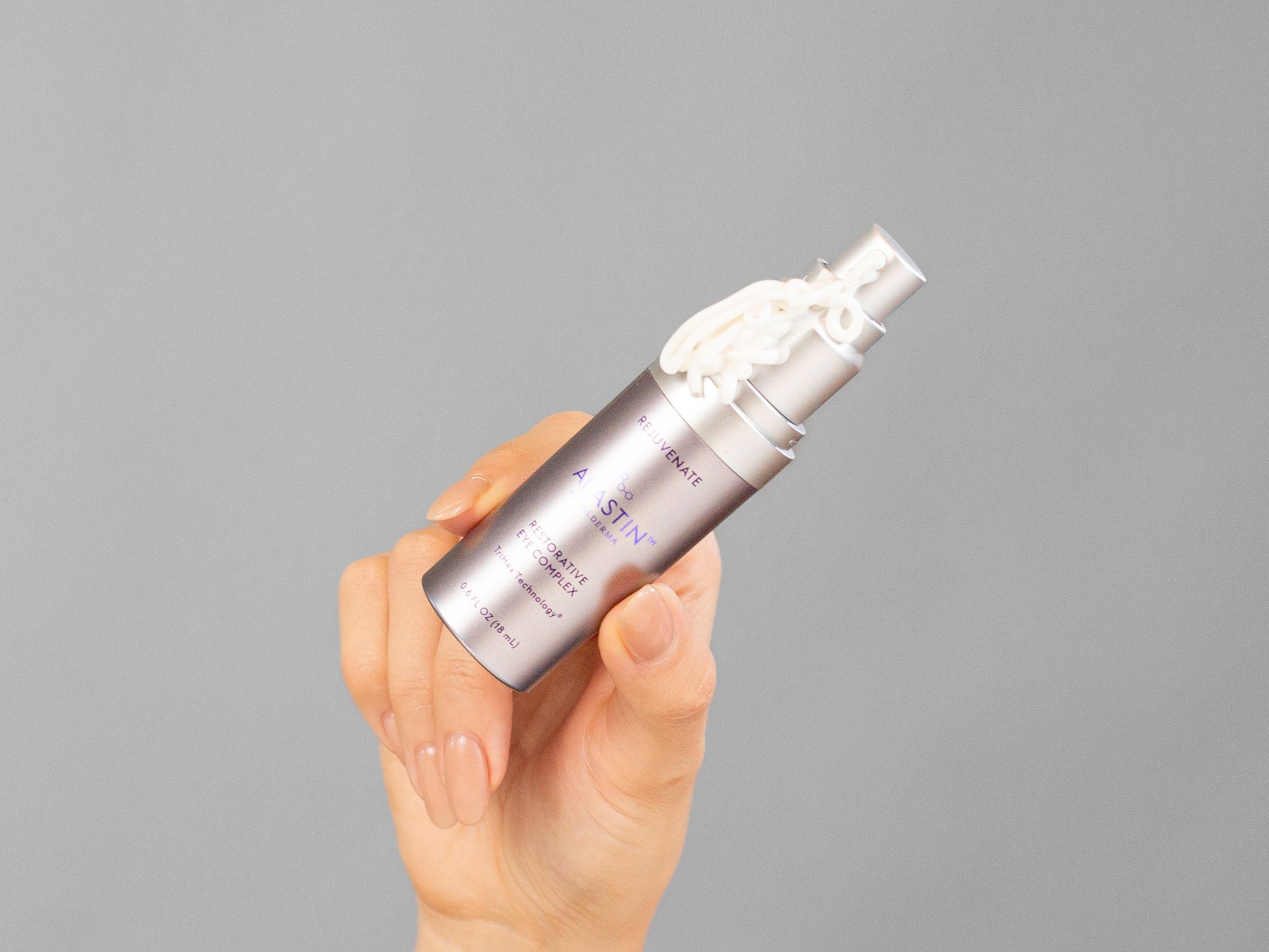 Laziza from LAZ Skincare holding an Alastin Restorative Eye Complex skincare bottle with a gray background