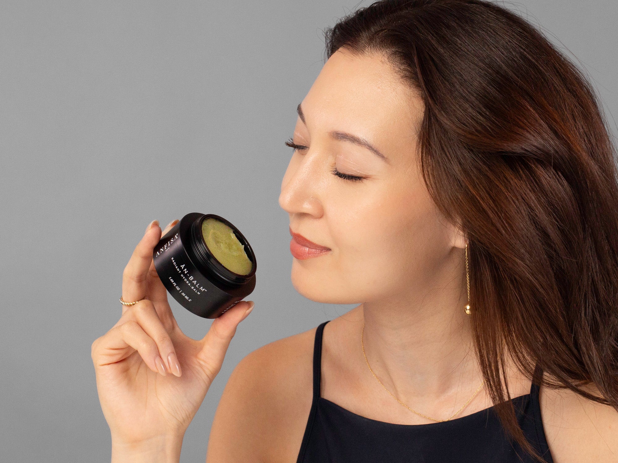 Laziza from LAZ Skincare showing the texture of Anfisa AN-BALM by holding an open jar up to her face