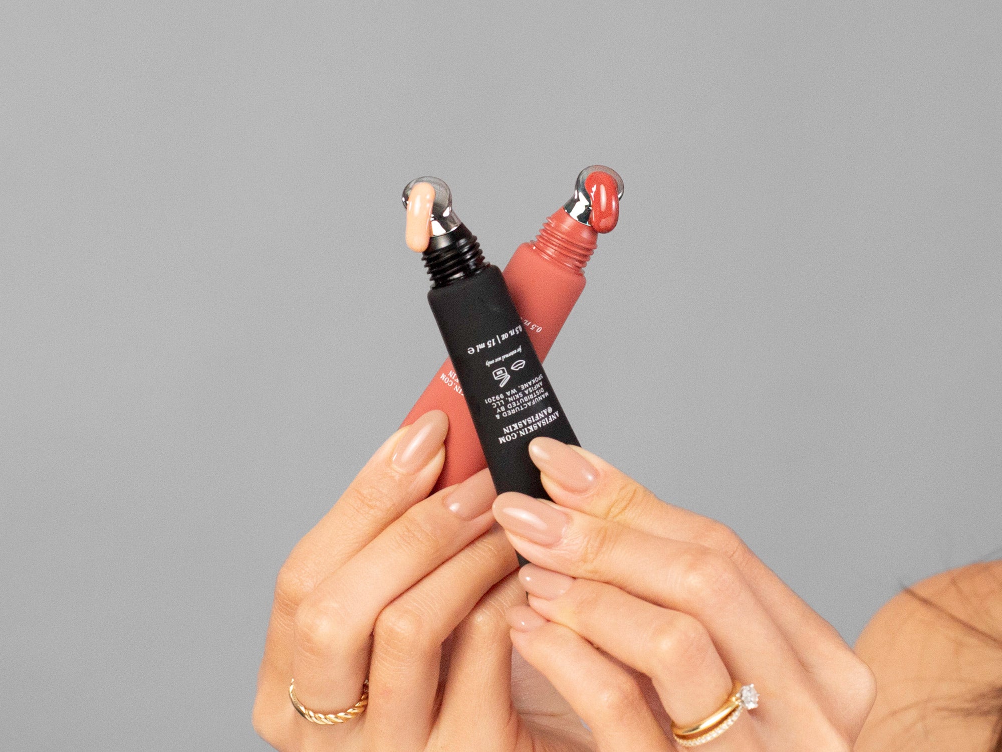 Closeup of Laziza from LAZ Skincare holding up 2 different colors of Anfisa AN-GLOSS in her hand