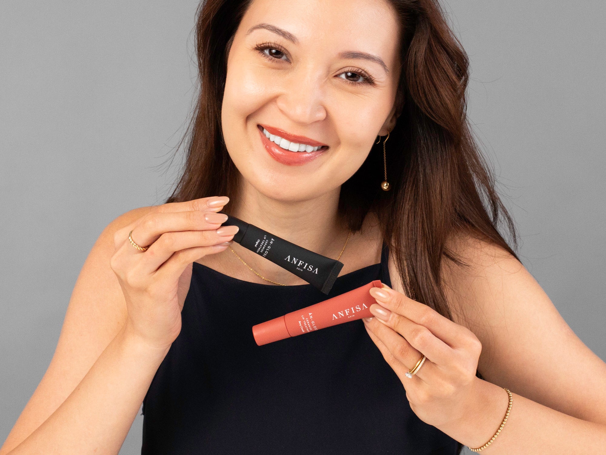 Laziza from LAZ Skincare holding up 2 different colored tubes of Anfisa AN-GLOSS in front of her face