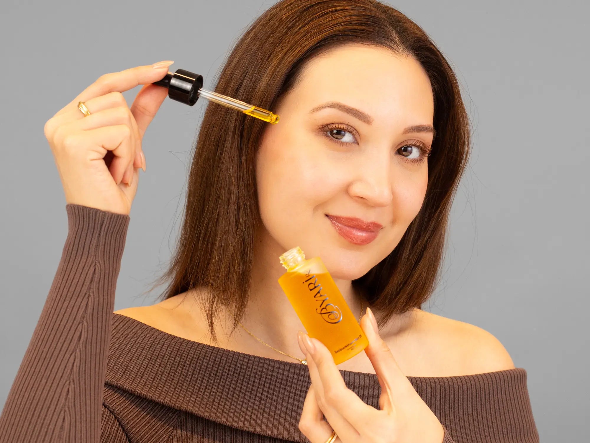 Laziza from LAZ Skincare holding a bottle of ByAri Rx Seabuckthorn Skin Oil up to her face
