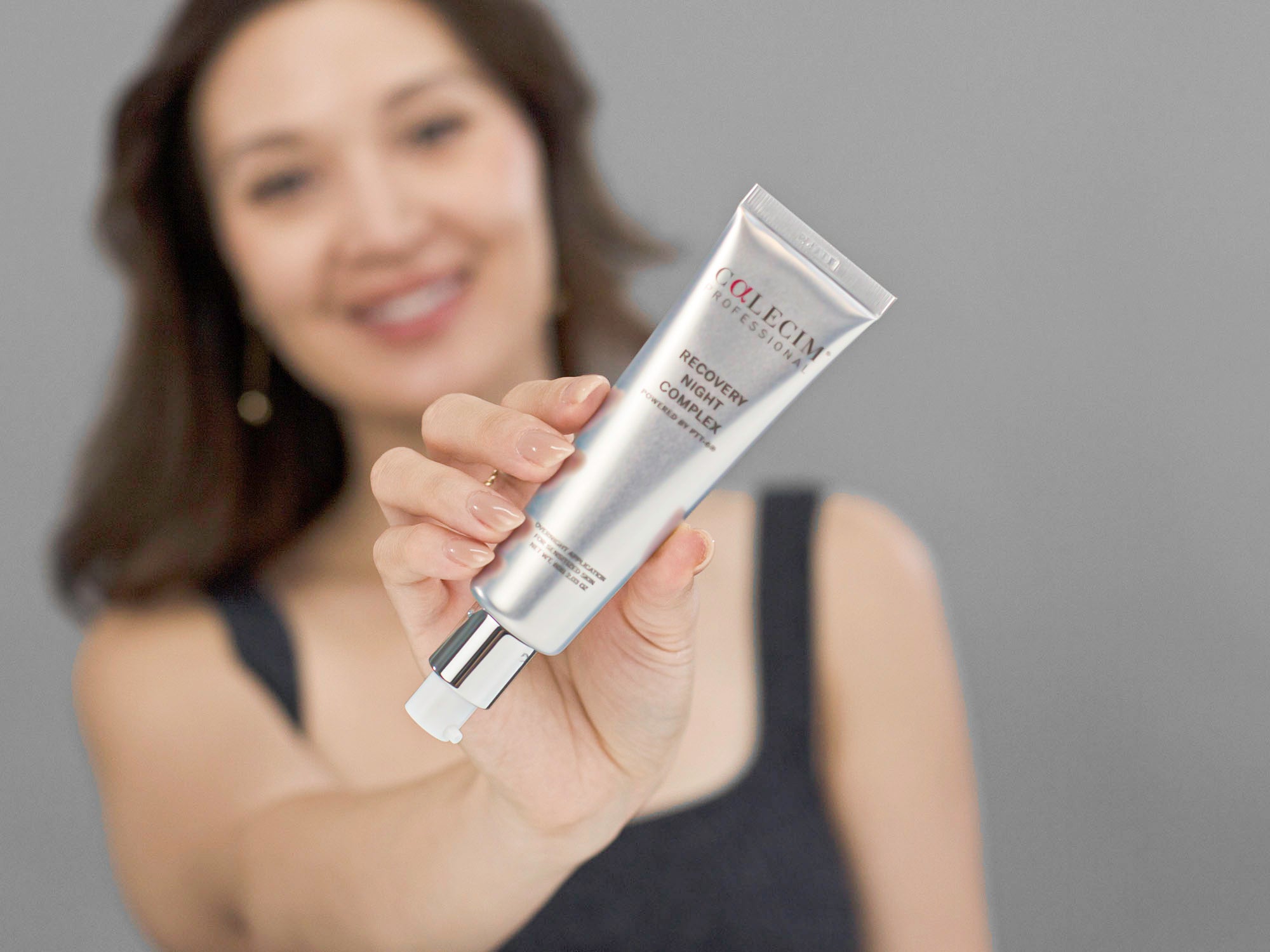 Laziza from LAZ Skincare holding a tube of Calecim Recovery Night Complex up to the camera with a blurred background