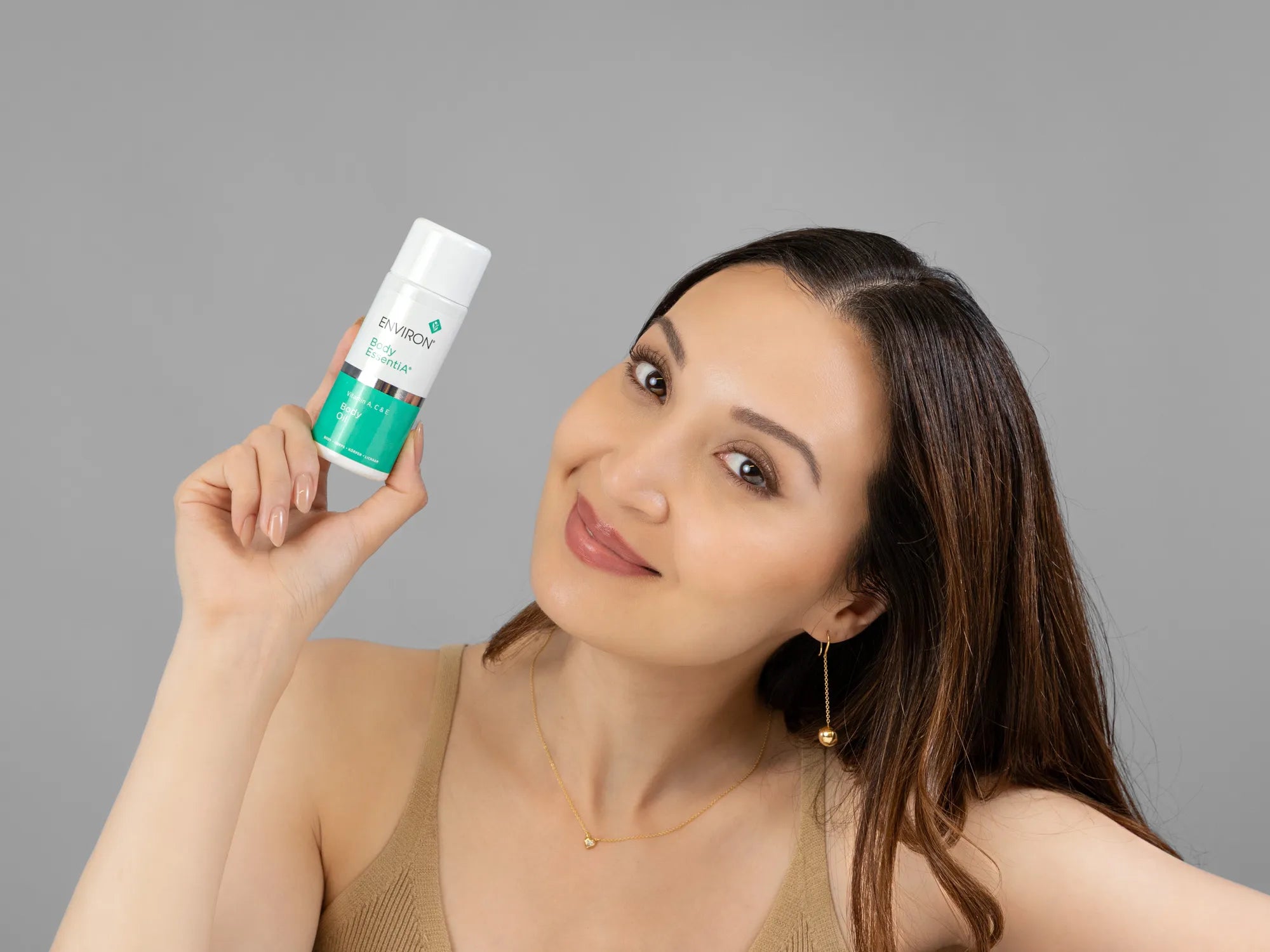 Laziza from LAZ Skincare holding a bottle of Environ Body Oil up to her face