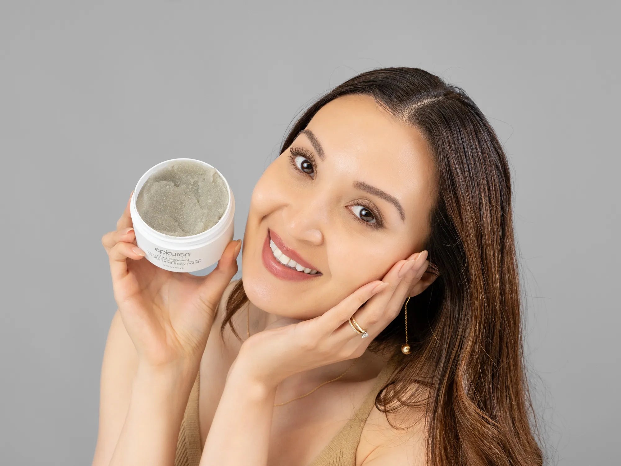 Laziza from LAZ Skincare holding a bottle of Epicuren Mint Renewal White Sand Body Polish up to her face