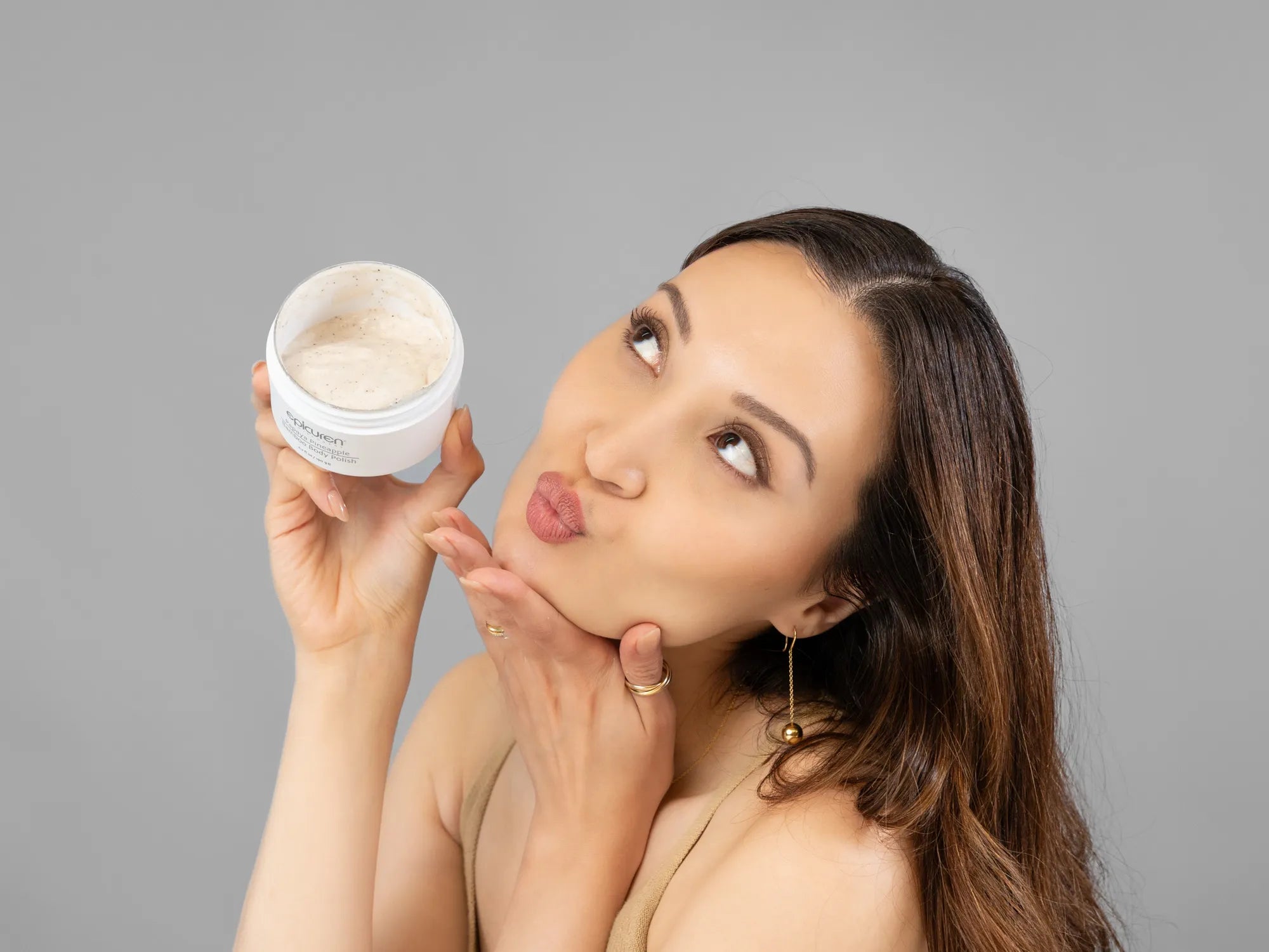 Laziza from LAZ Skincare holding a bottle of Epicuren Papaya Pineapple Bamboo Body Polish up to her face