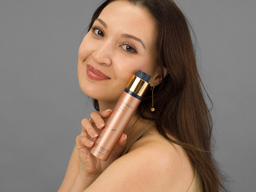 Laziza from LAZ Skincare holding a bottle of SkinBetter Science Even Tone Correcting Serum up to her face