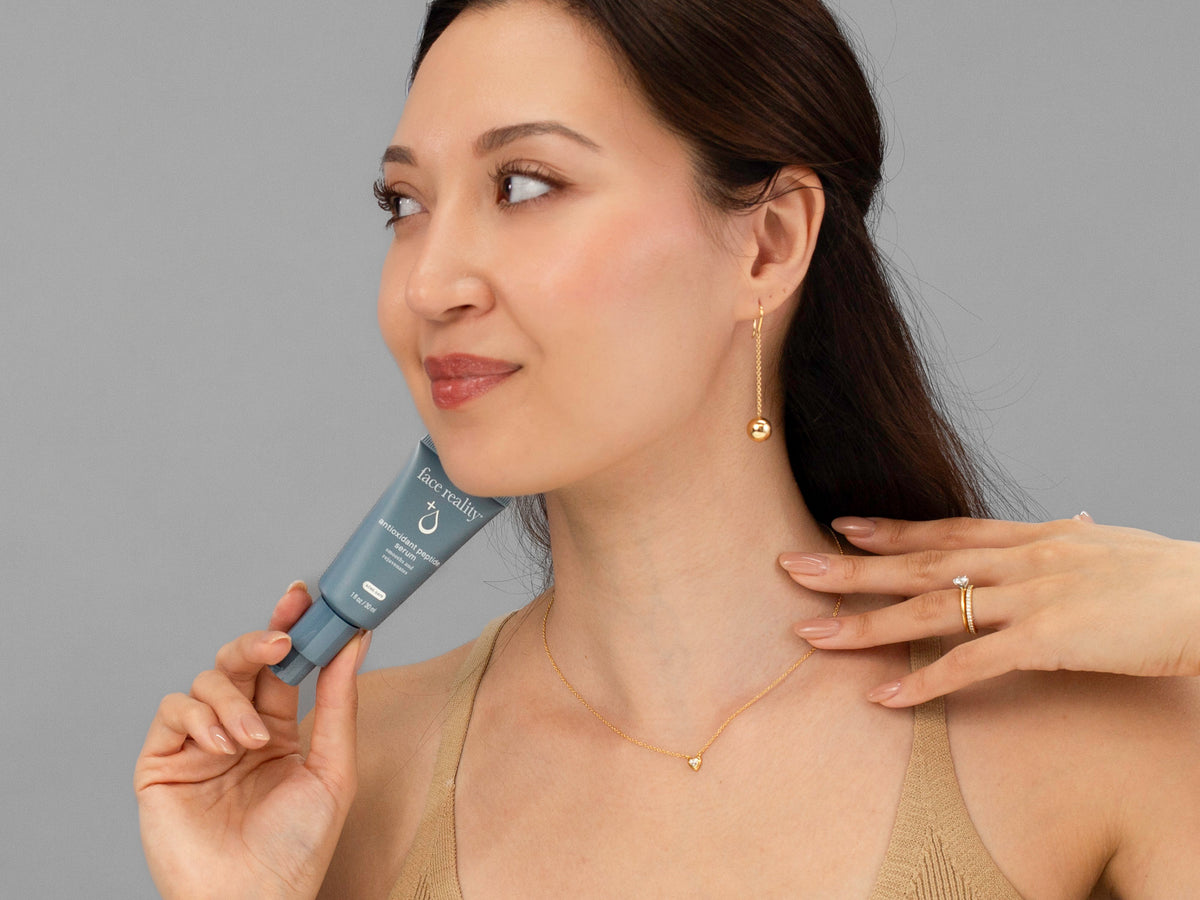 Laziza from LAZ Skincare holding a bottle of Face Reality Antioxidant Peptide Serum up to her face