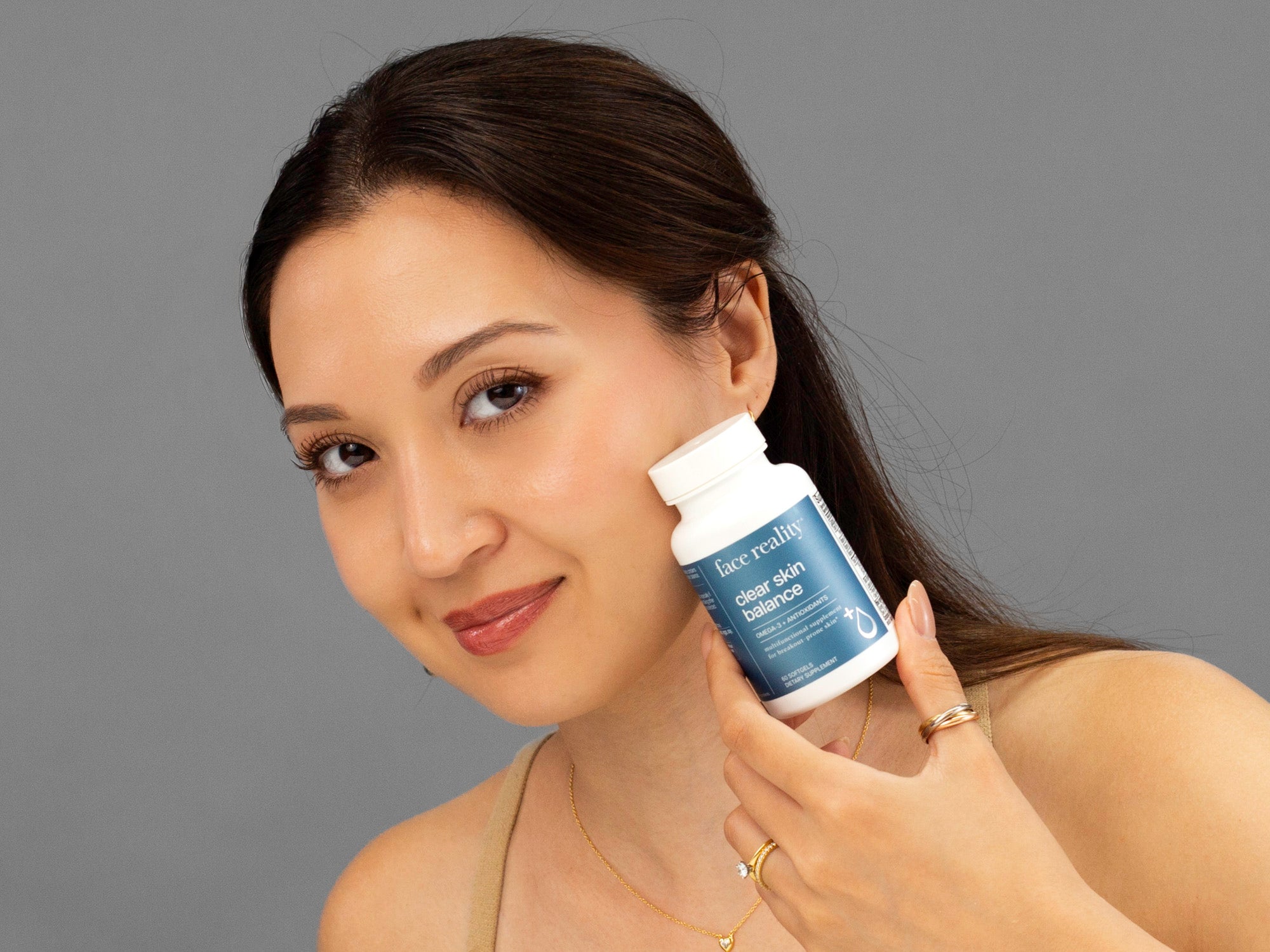 Laziza from LAZ Skincare holding a bottle of Face Reality Clear Skin Balance supplements up to her face
