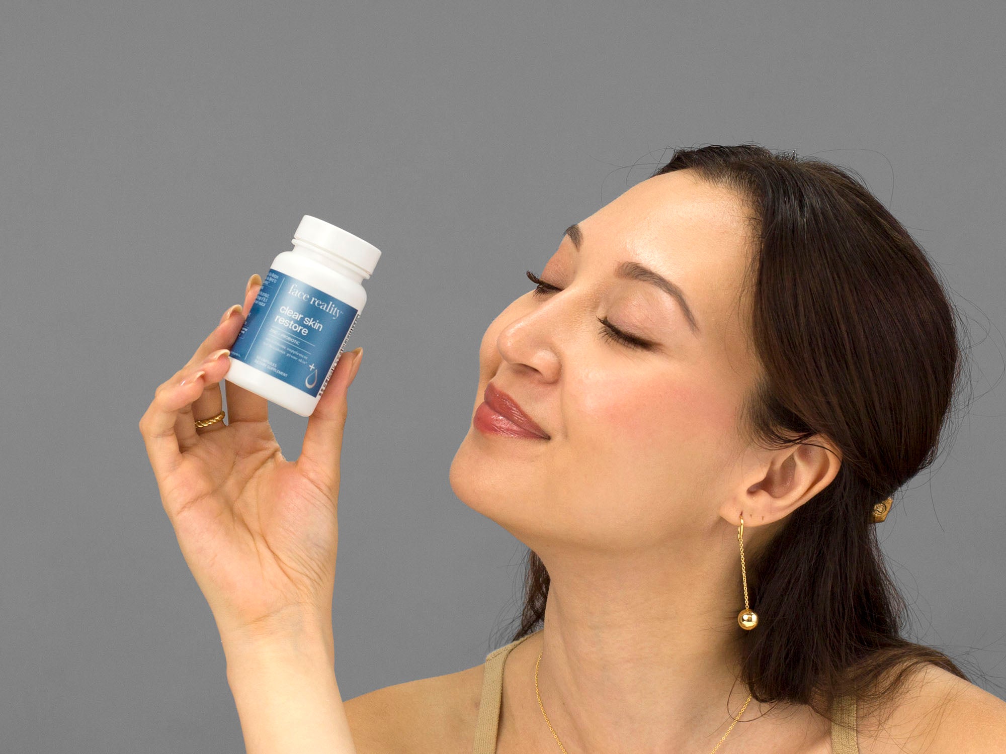 Laziza from LAZ Skincare holding a bottle of Face Reality Clear Skin Restore up to her face