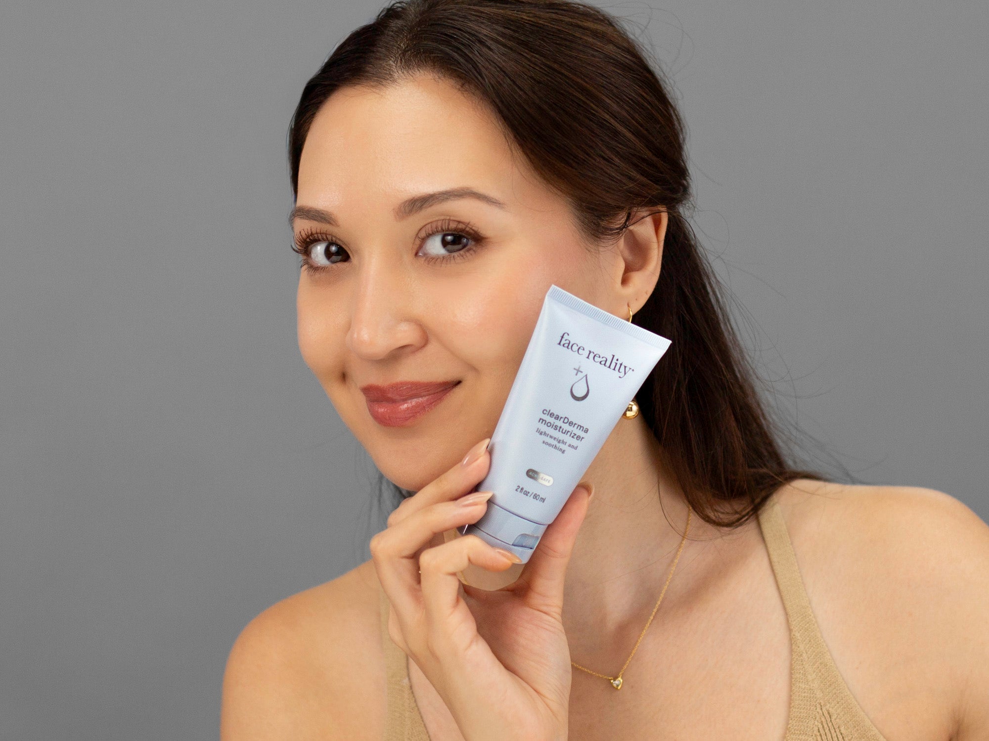 Laziza from LAZ Skincare holding a bottle of Face Reality Clearderma Moisturizer up to her face