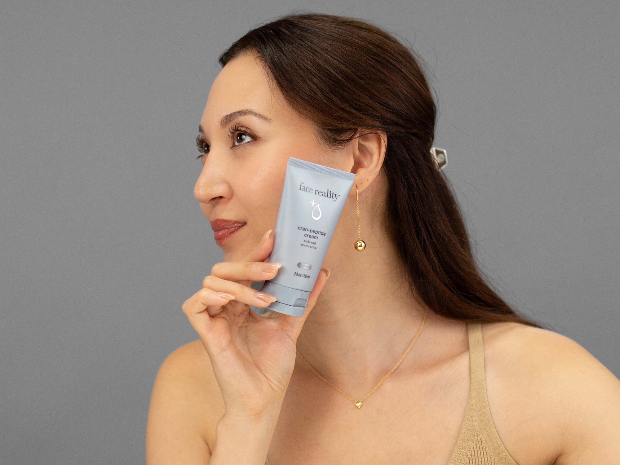 Laziza from LAZ Skincare holding a bottle of Face Reality Cran-Peptide Cream up to her face