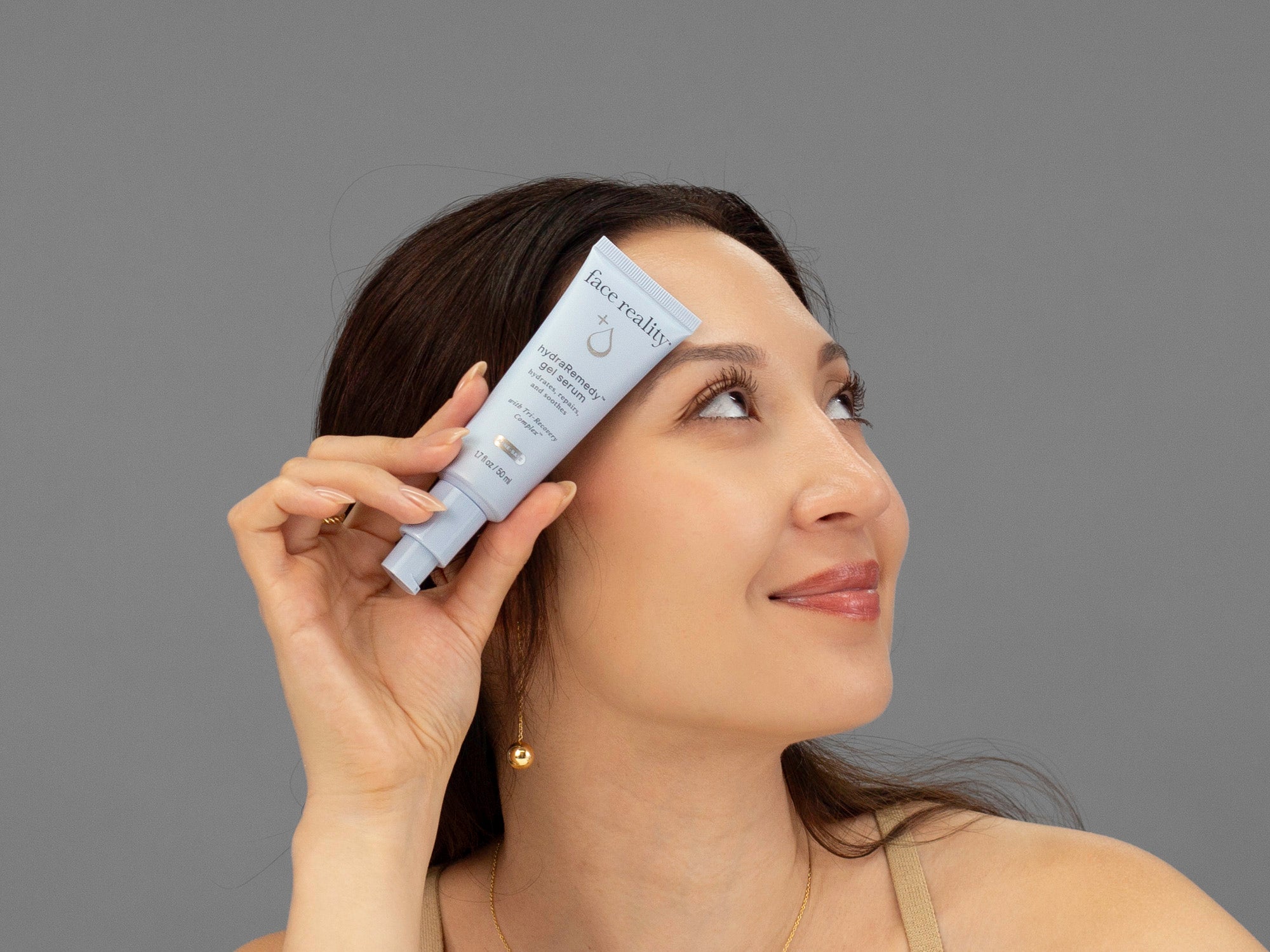 Laziza from LAZ Skincare holding a tube of Face Reality HydraRemedy Gel Serum up to her face