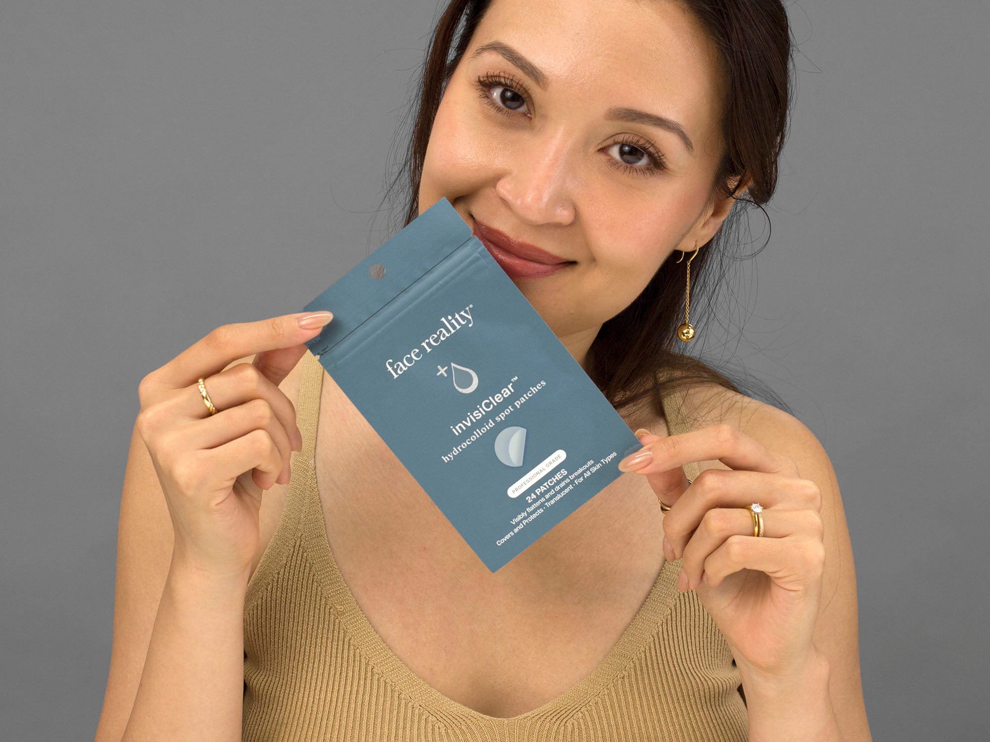 Laziza from LAZ Skincare holding a bottle of Face Reality InvisiClear Hydrocolloid Spot Patches up to her face
