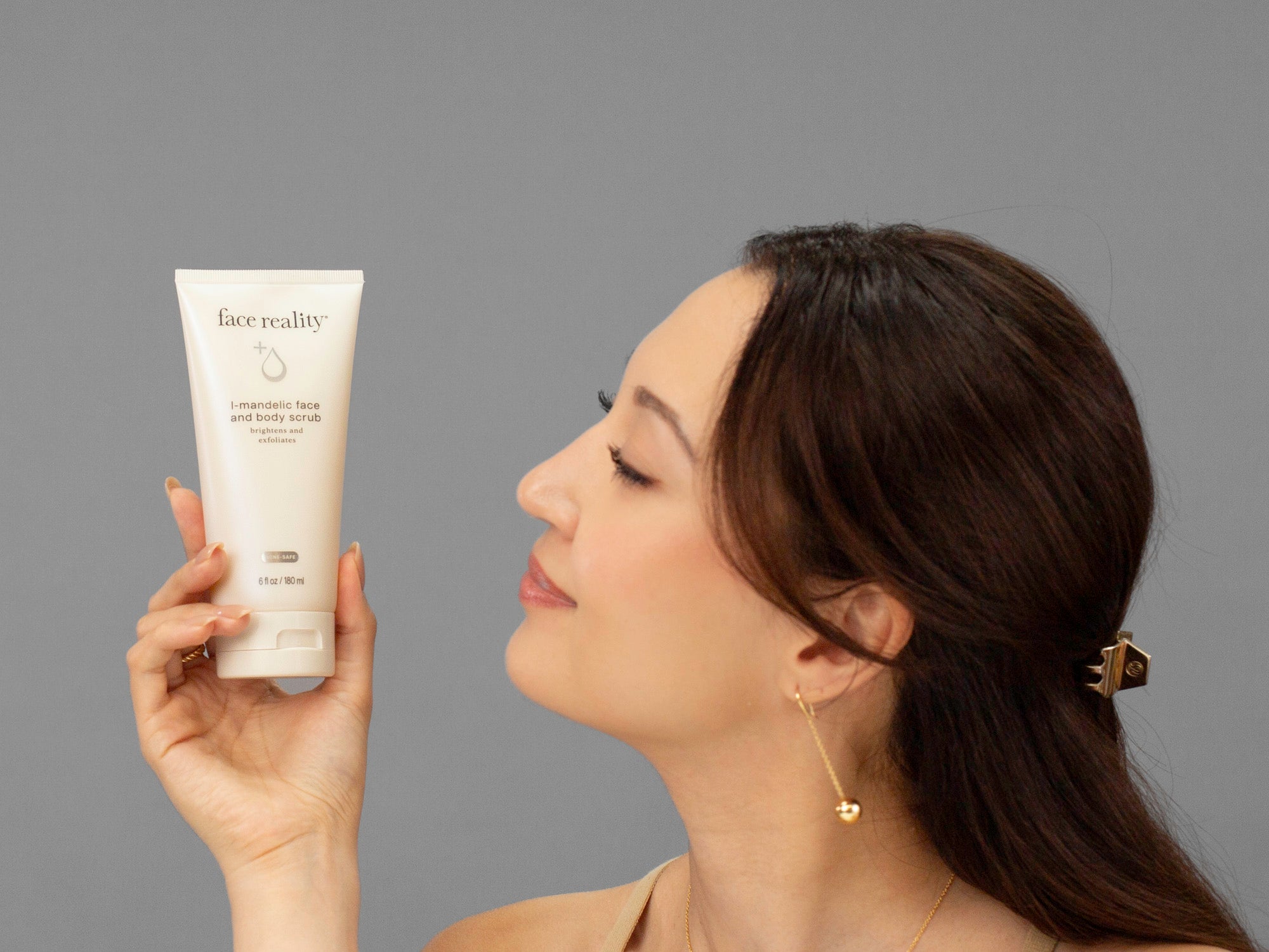 Laziza from LAZ Skincare holding a tube of Face Reality Mandelic Face & Body scrub up to her face