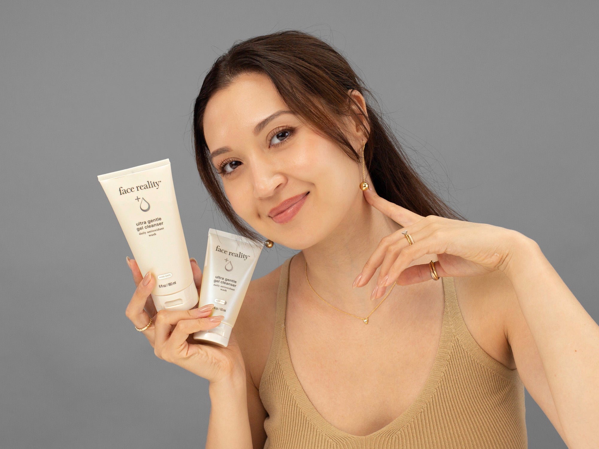 Laziza from LAZ Skincare holding two sizes of bottles of Face Reality Ultra Gentle Gel Cleanser in her hand