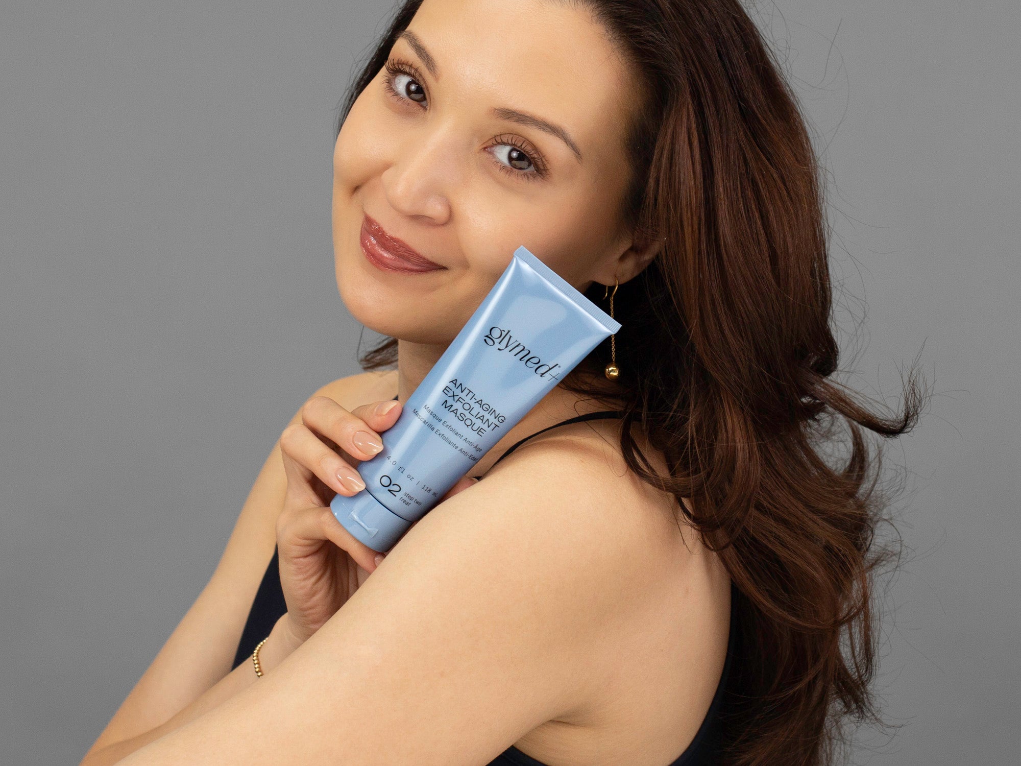 Closeup of Laziza from LAZ Skincare holding a tube of GlyMed Anti-Aging Exfoliant Masque up to her face