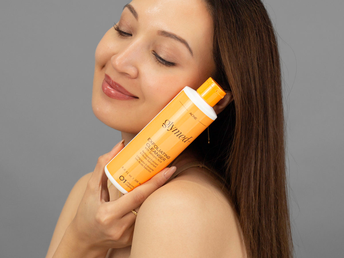 Laziza from LAZ Skincare holding a bottle of GlyMed Exfoliating Cleanser up to her face