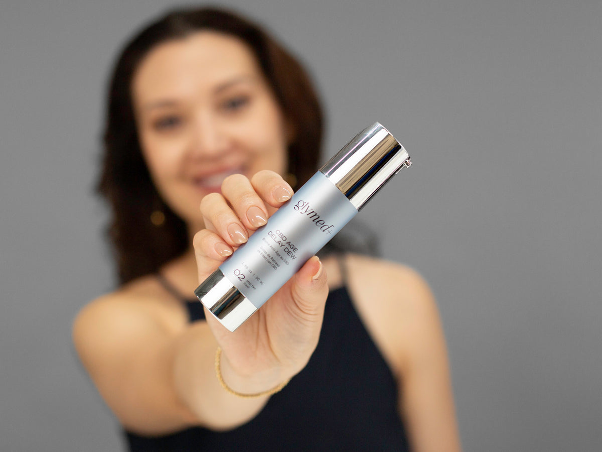 Laziza from LAZ Skincare holding a bottle of GlyMed Hemp Age Delay Dew up to her face