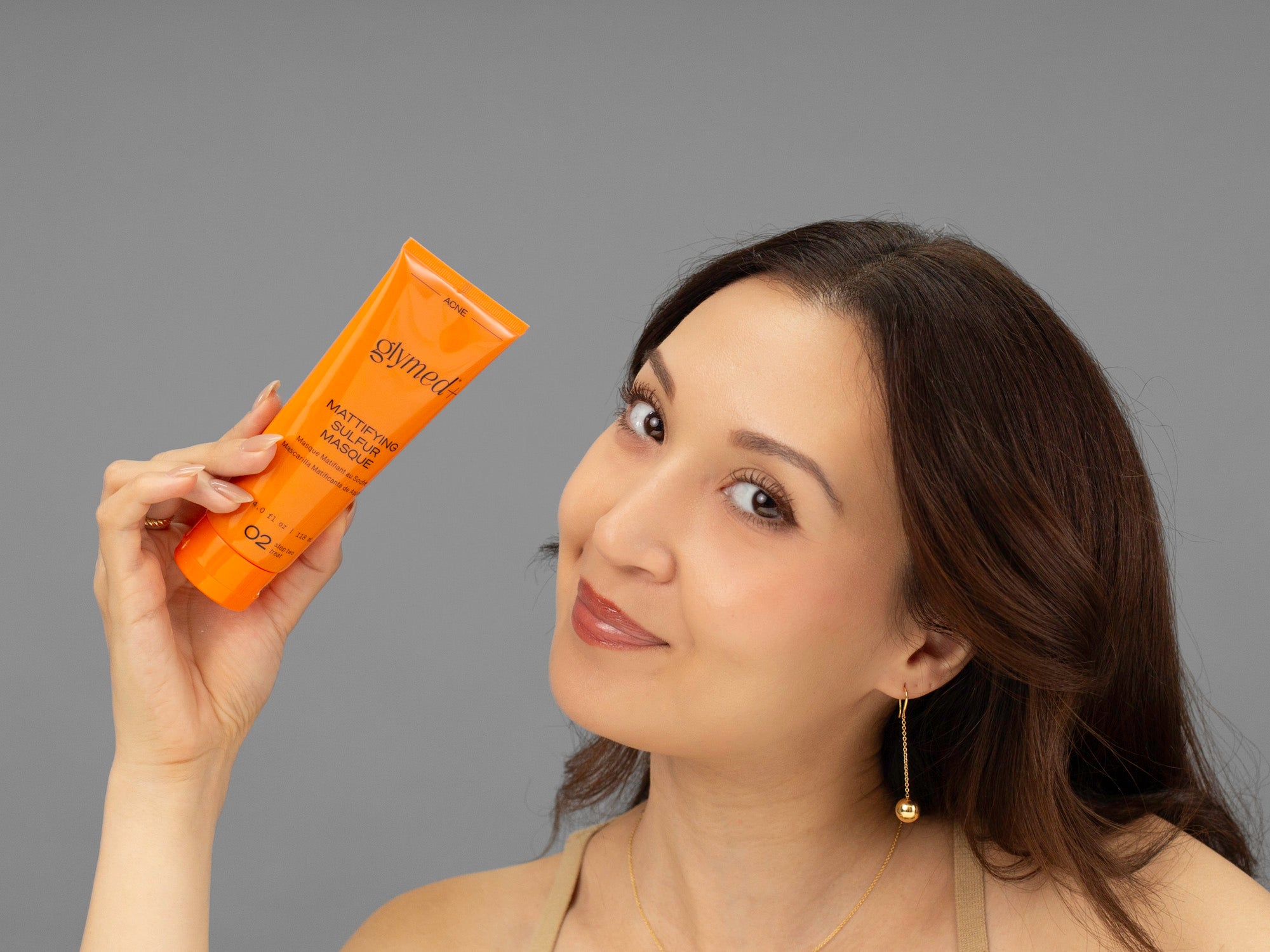 Laziza from LAZ Skincare holding a bottle of GlyMed Mattifying Sulfur Masque up to her face