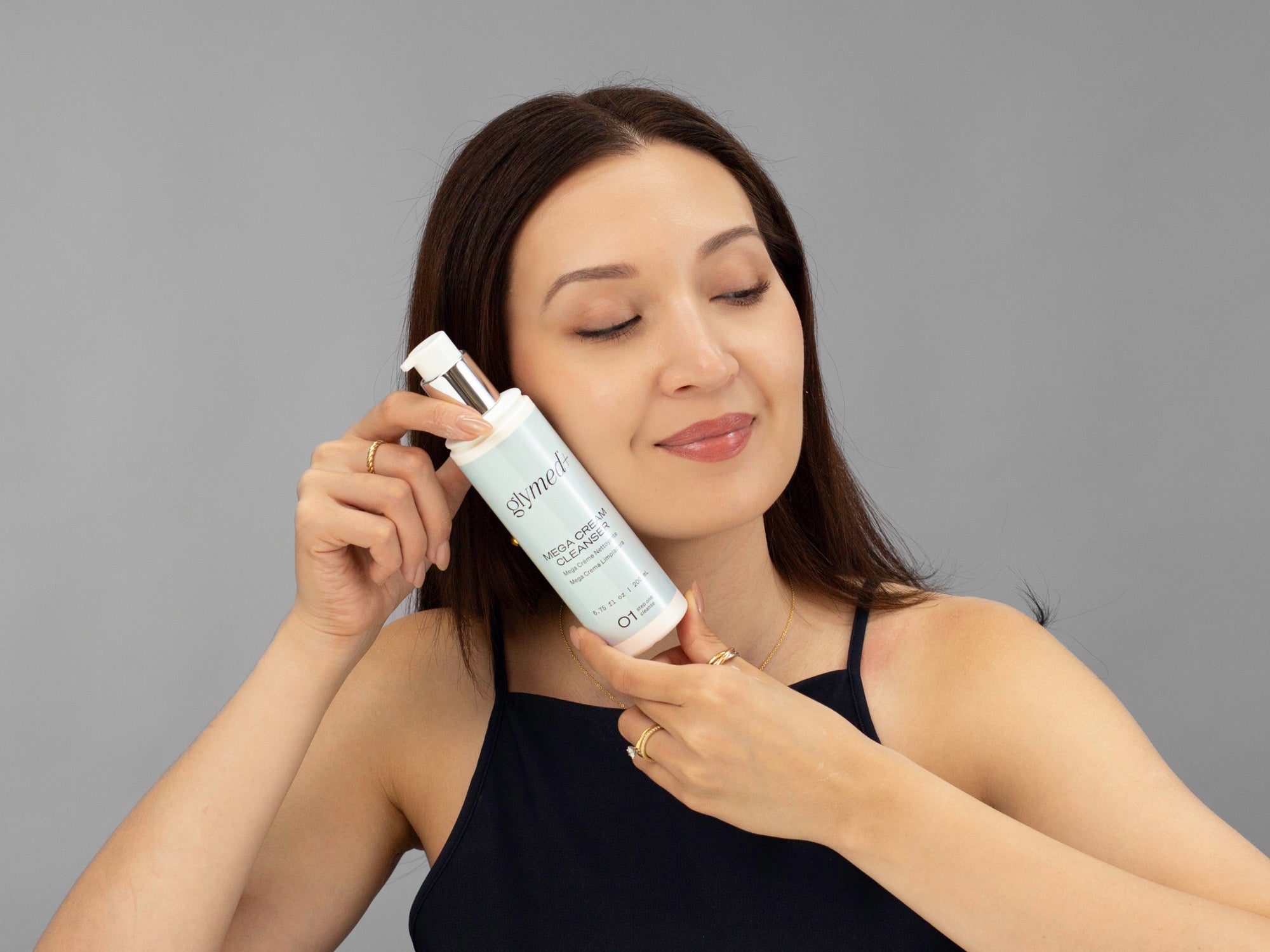 Laziza from LAZ Skincare holding a bottle of GlyMed Mega Cream Cleanser up to her face