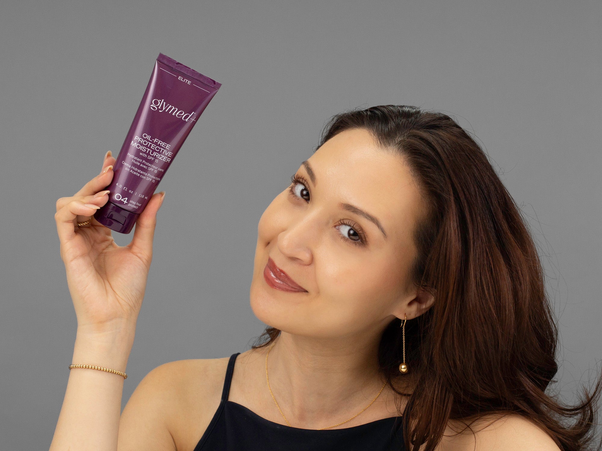 Laziza from LAZ Skincare holding a tube of GlyMed Oil-Free Protective Moisturizer in her hand