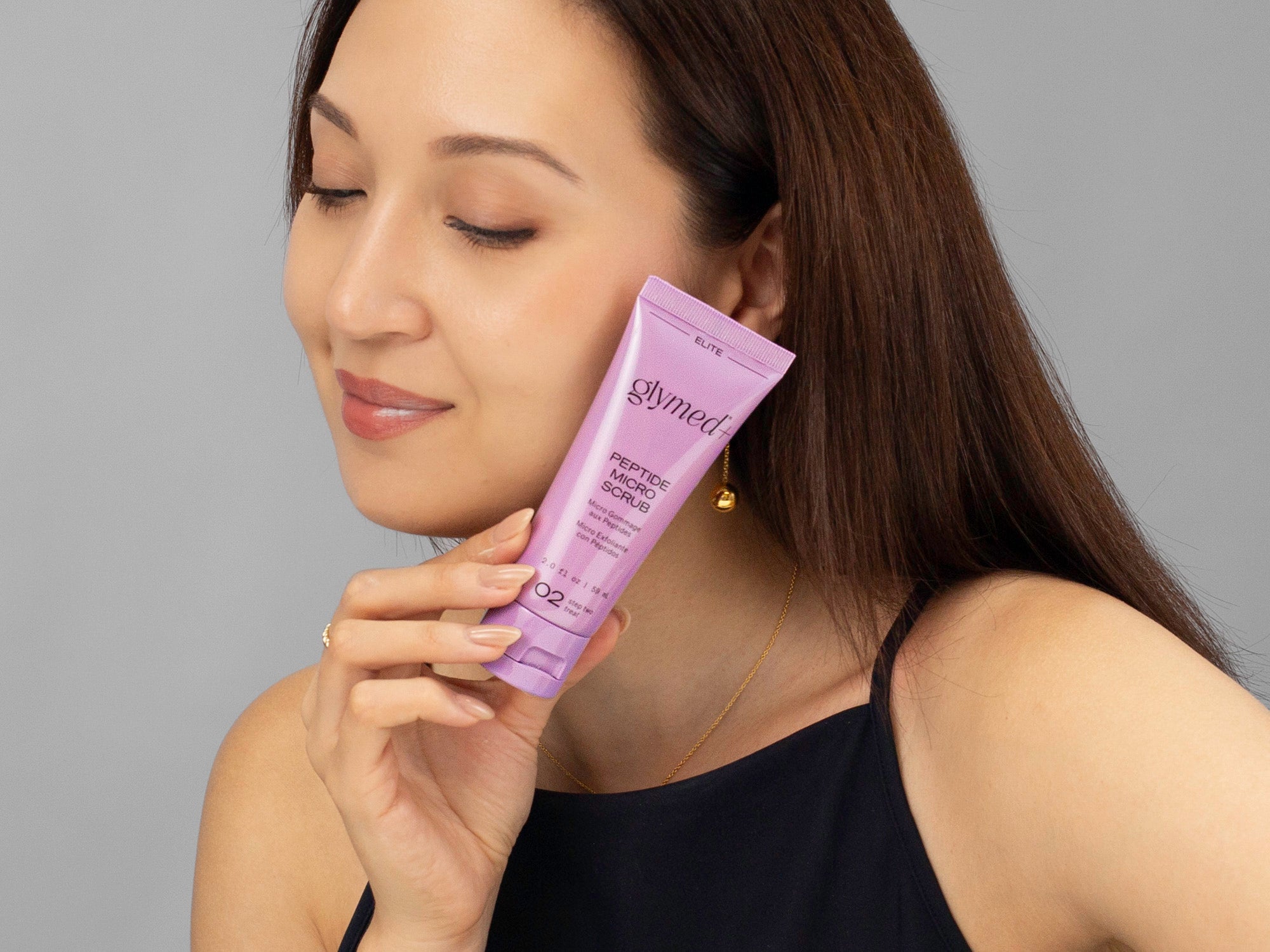Laziza from LAZ Skincare holding a bottle of GlyMed Peptide Micro Scrub up to her face