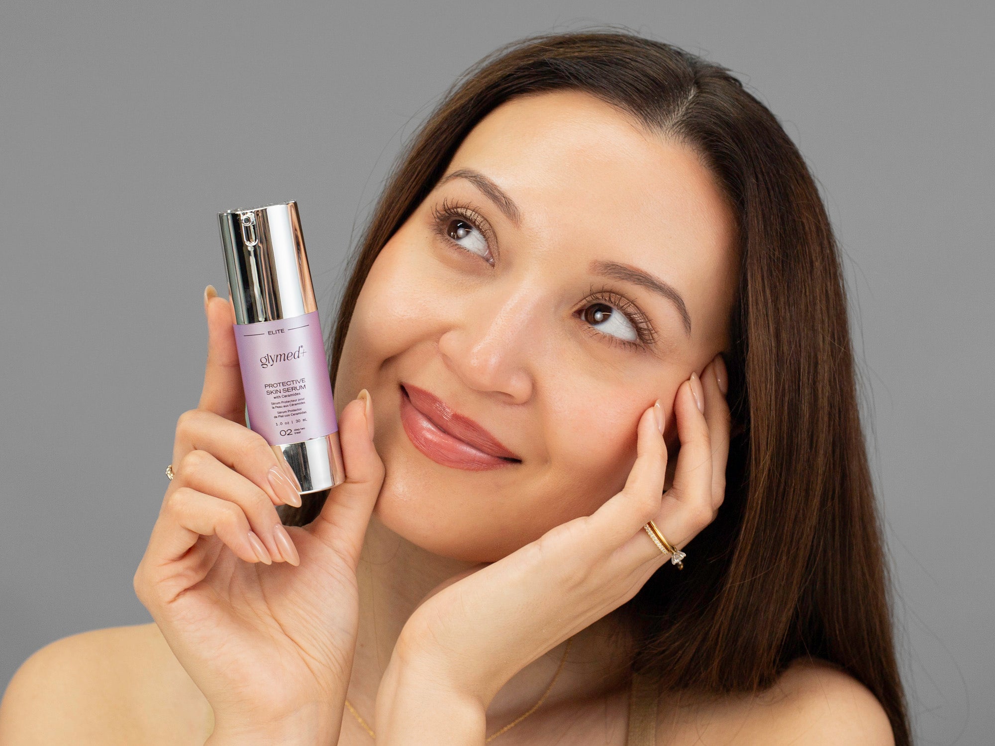 Laziza from LAZ Skincare holding a bottle of GlyMed Protective Skin Serum up to her face