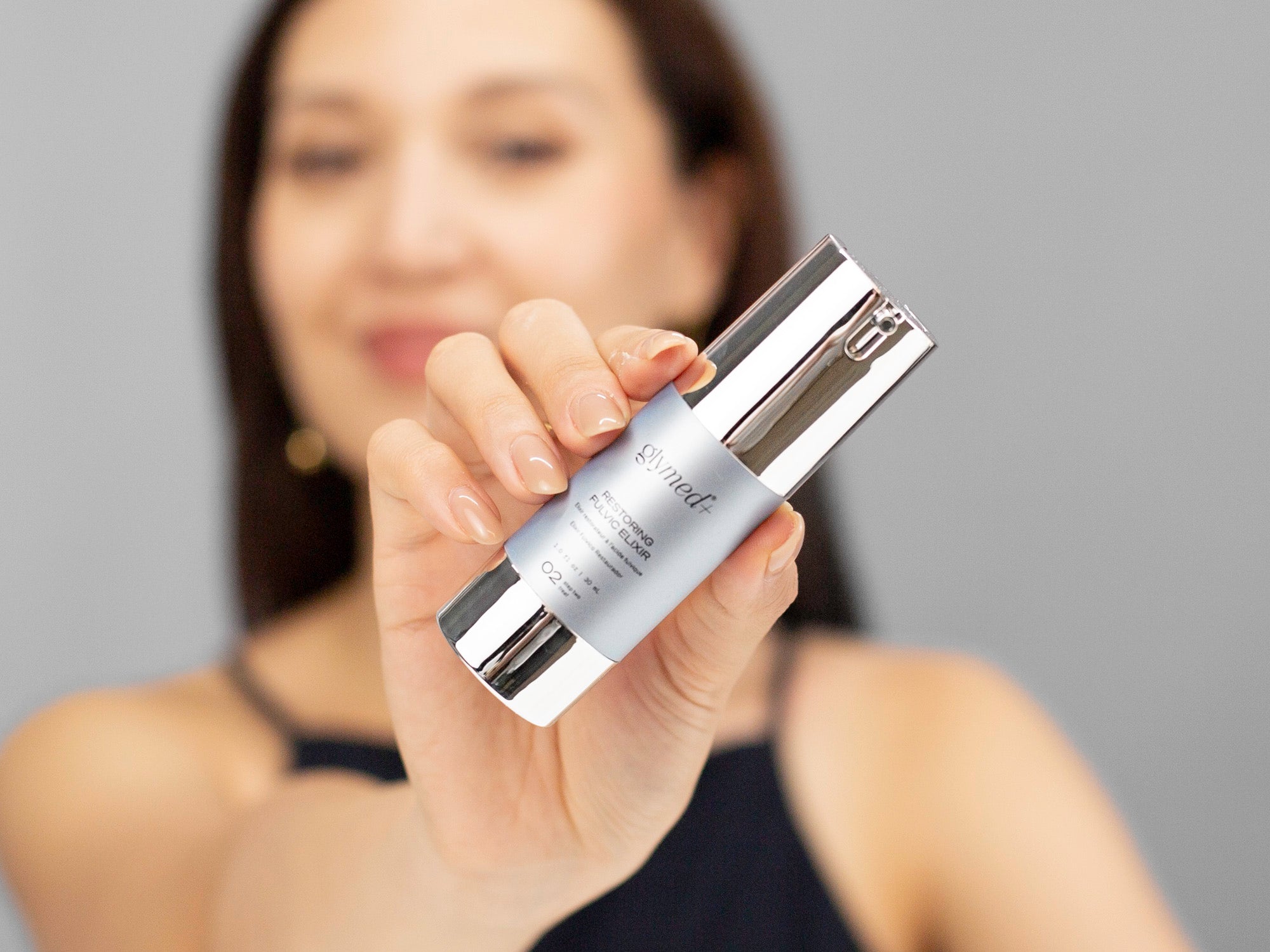 Laziza from LAZ Skincare holding up a bottle of GlyMed Restoring Fulvic Elixir with a blurred background