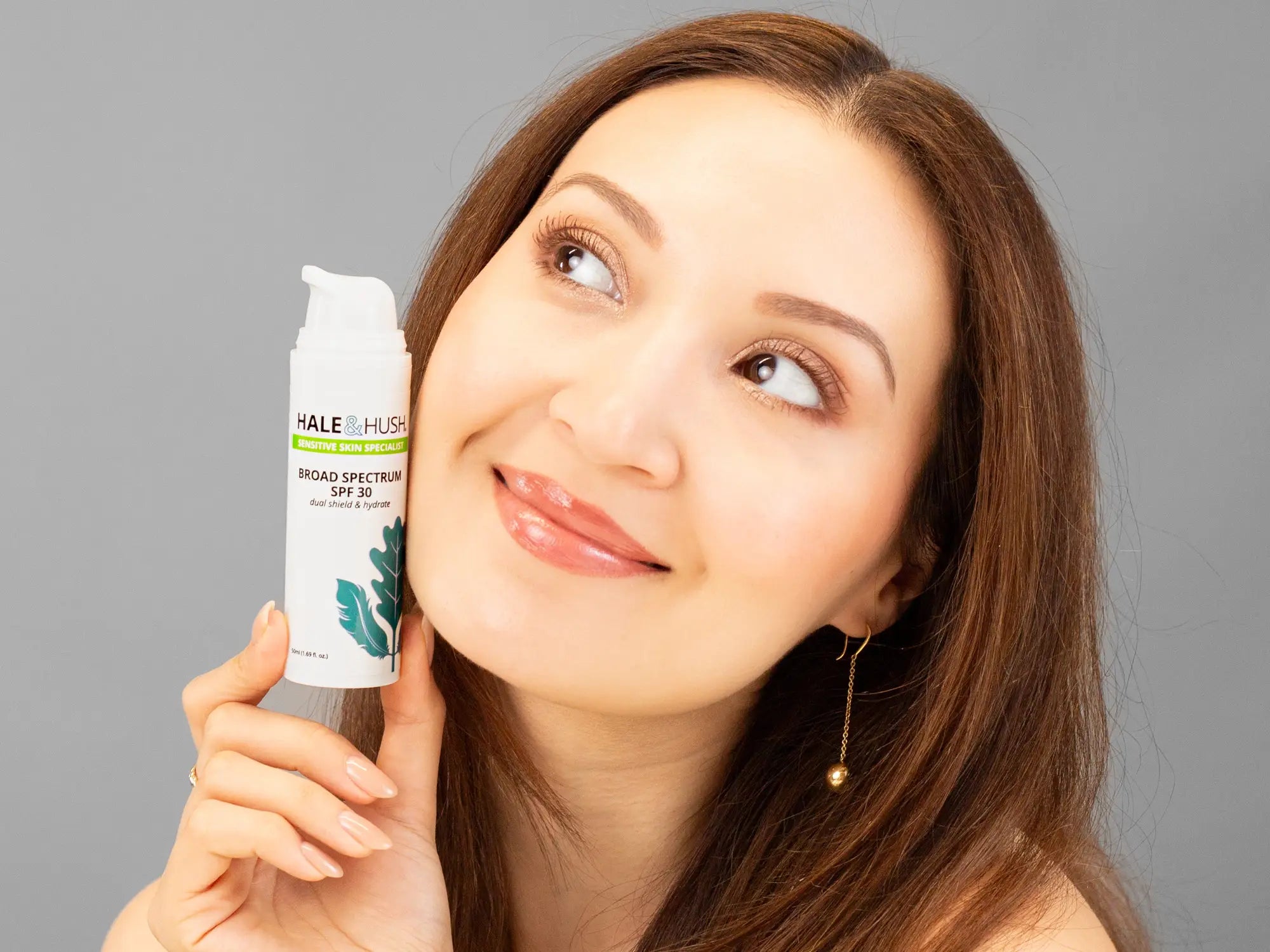 Laziza from LAZ Skincare holding a bottle of Hale & Hush Broad Spectrum Natural SPF30 up to her face