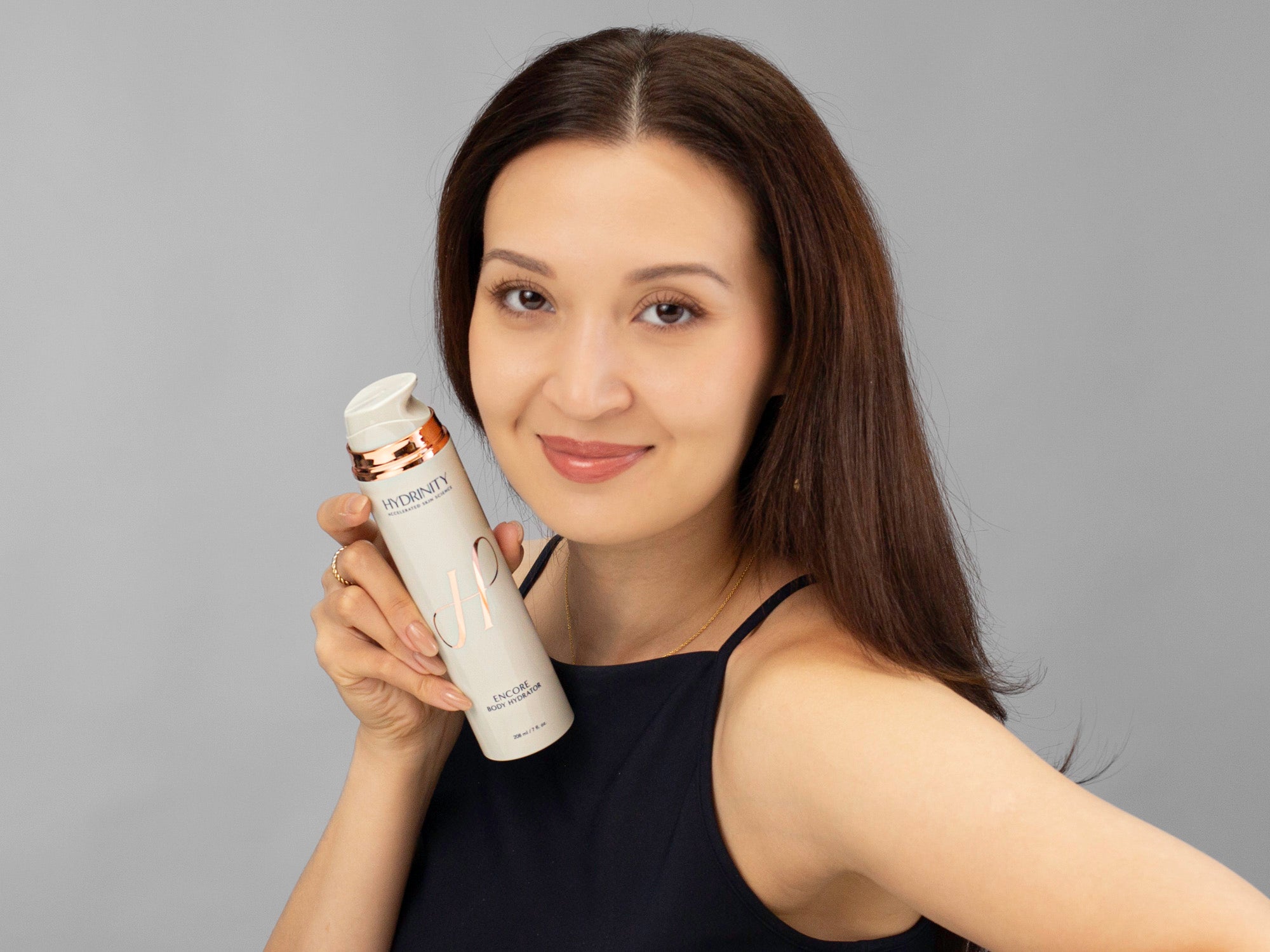 Laziza from LAZ Skincare holding a bottle of Hydrinity Encore Body Hydrator next to her face