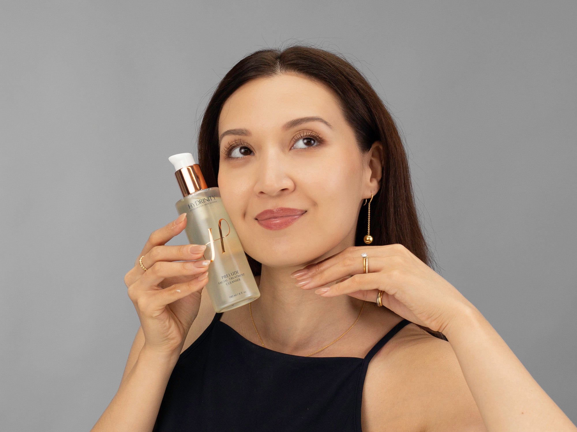 Laziza from LAZ Skincare holding a bottle of Hydrinity Prelude Facial Treatment Cleanser close to her face