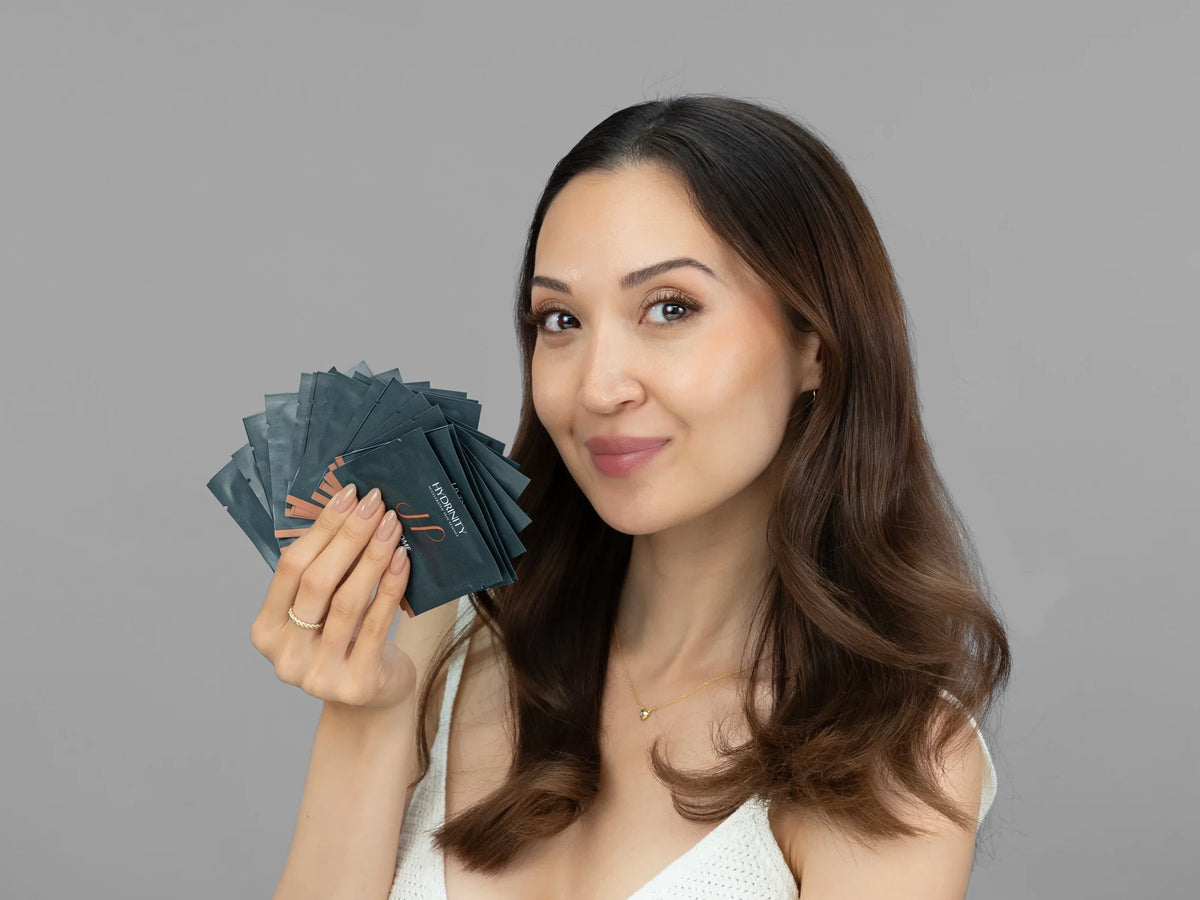 Laziza from LAZ Skincare holding a bottle of Hydrinity RetaXome Retinal Boost Treatment Pads up to her face