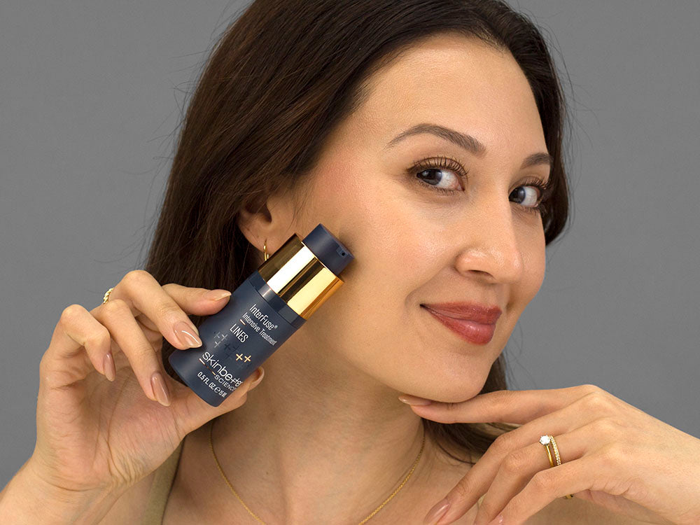 Laziza from LAZ Skincare holding a bottle of SkinBetter Science InterFuse Intensive Treatment LINES up to her face