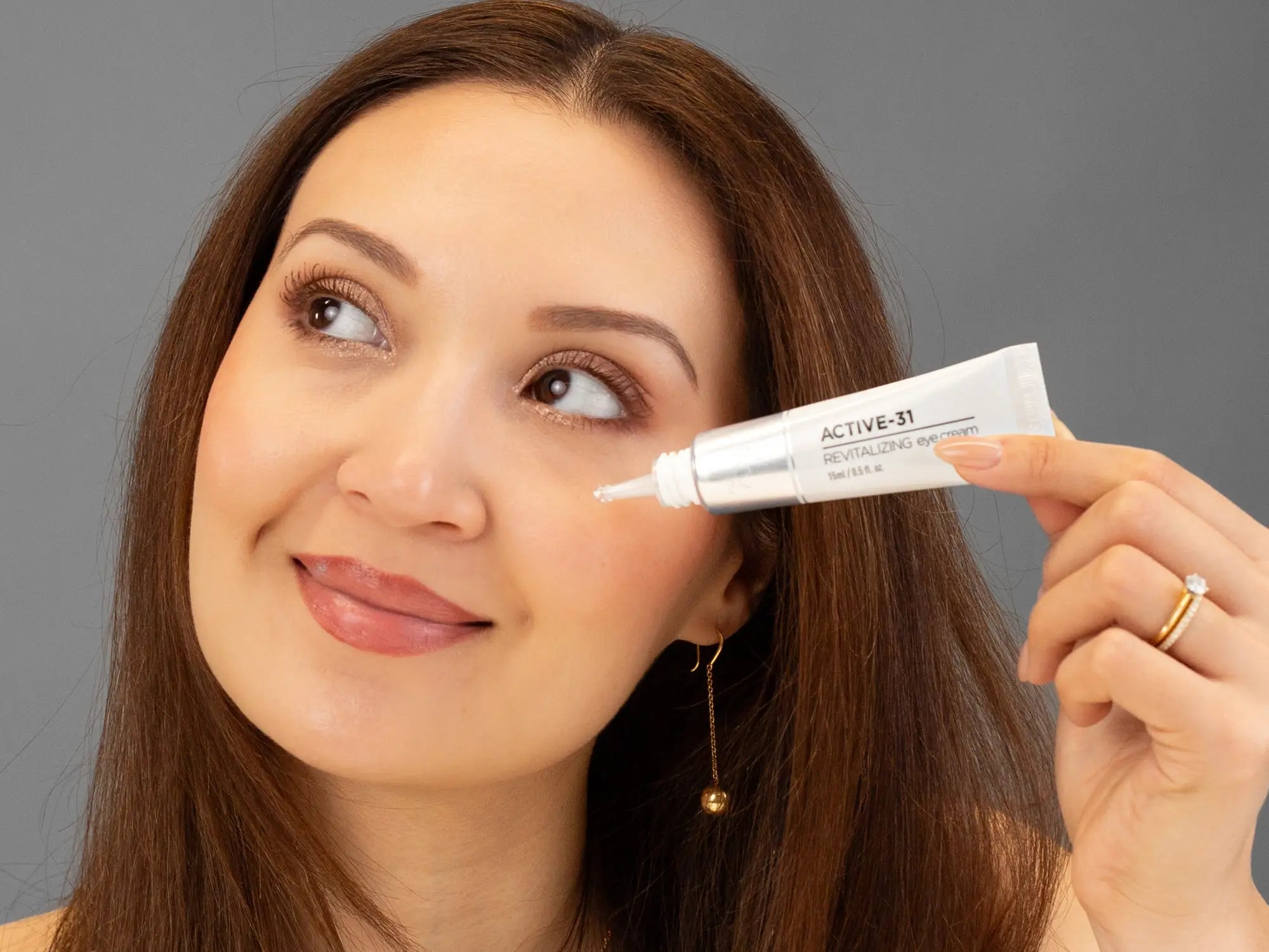 Laziza from LAZ Skincare holding a bottle of KrX Aesthetics Active 31 Revitalizing Eye Cream up to her face