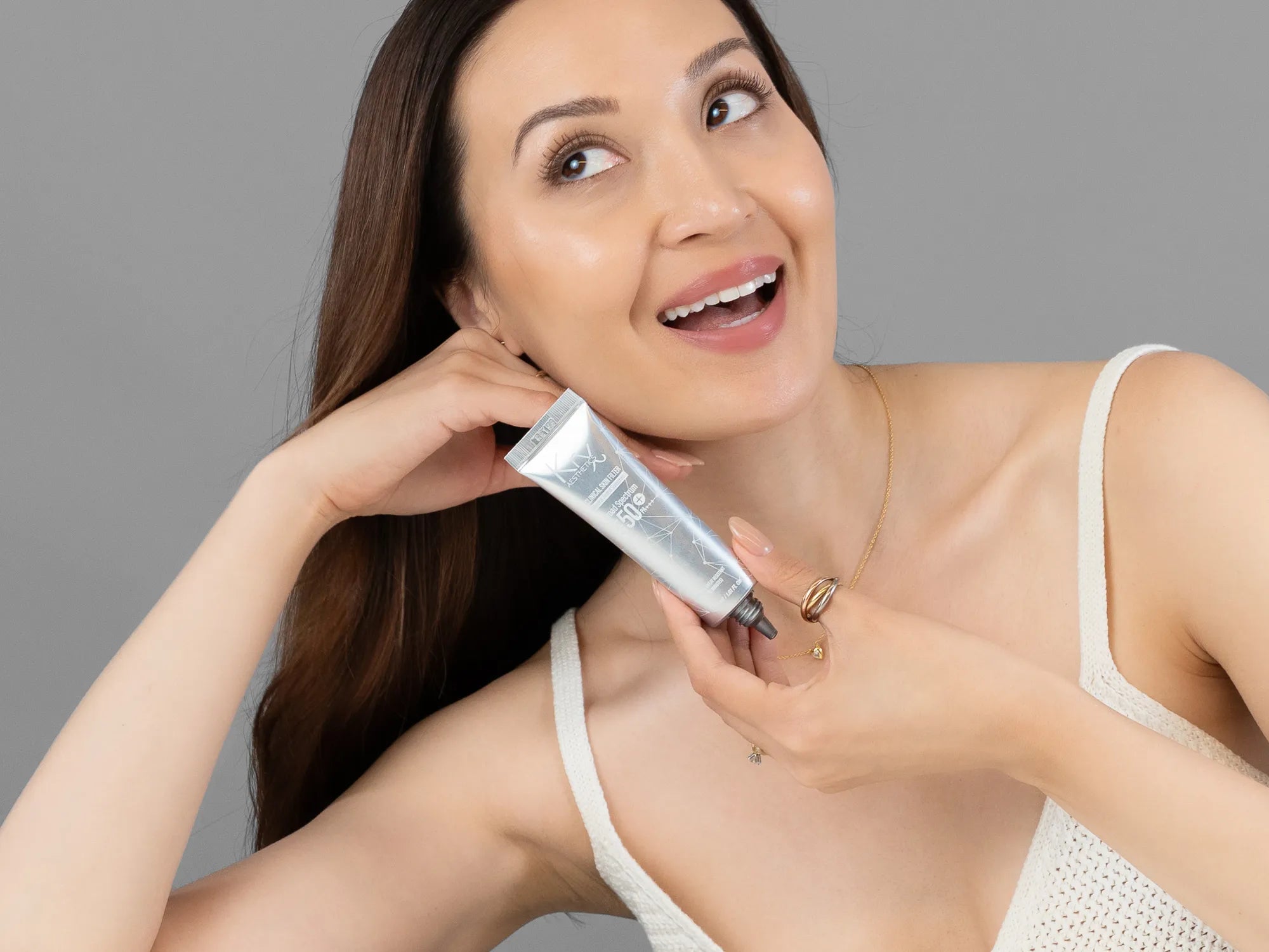 Laziza from LAZ Skincare holding a bottle of KrX Aesthetics Skin Filter Tinted Sunscreen SPF 50 up to her face
